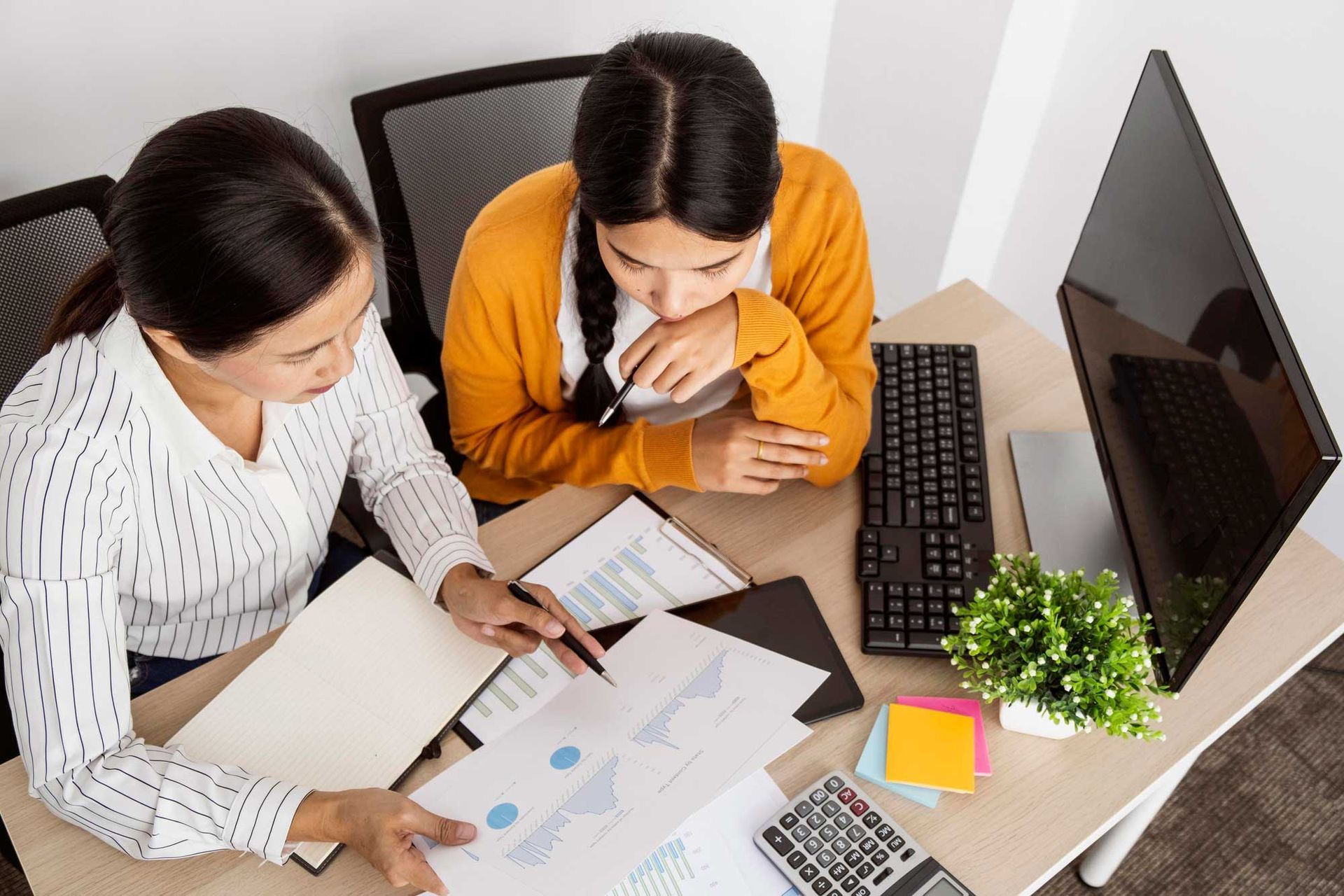 Two women are sitting at a desk looking at a computer screen.