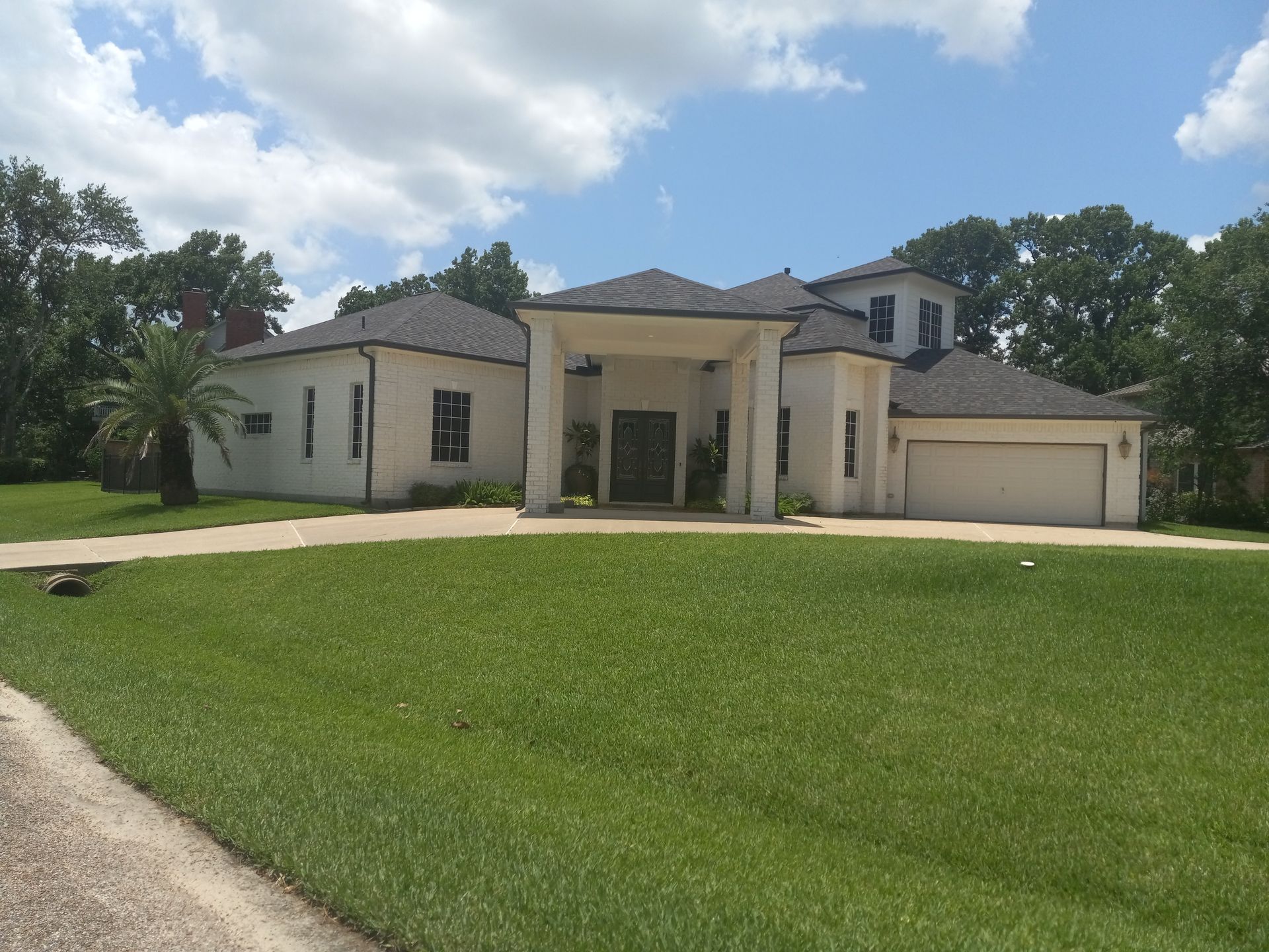 White stucco house with a green lawn and driveway under a blue sky.
