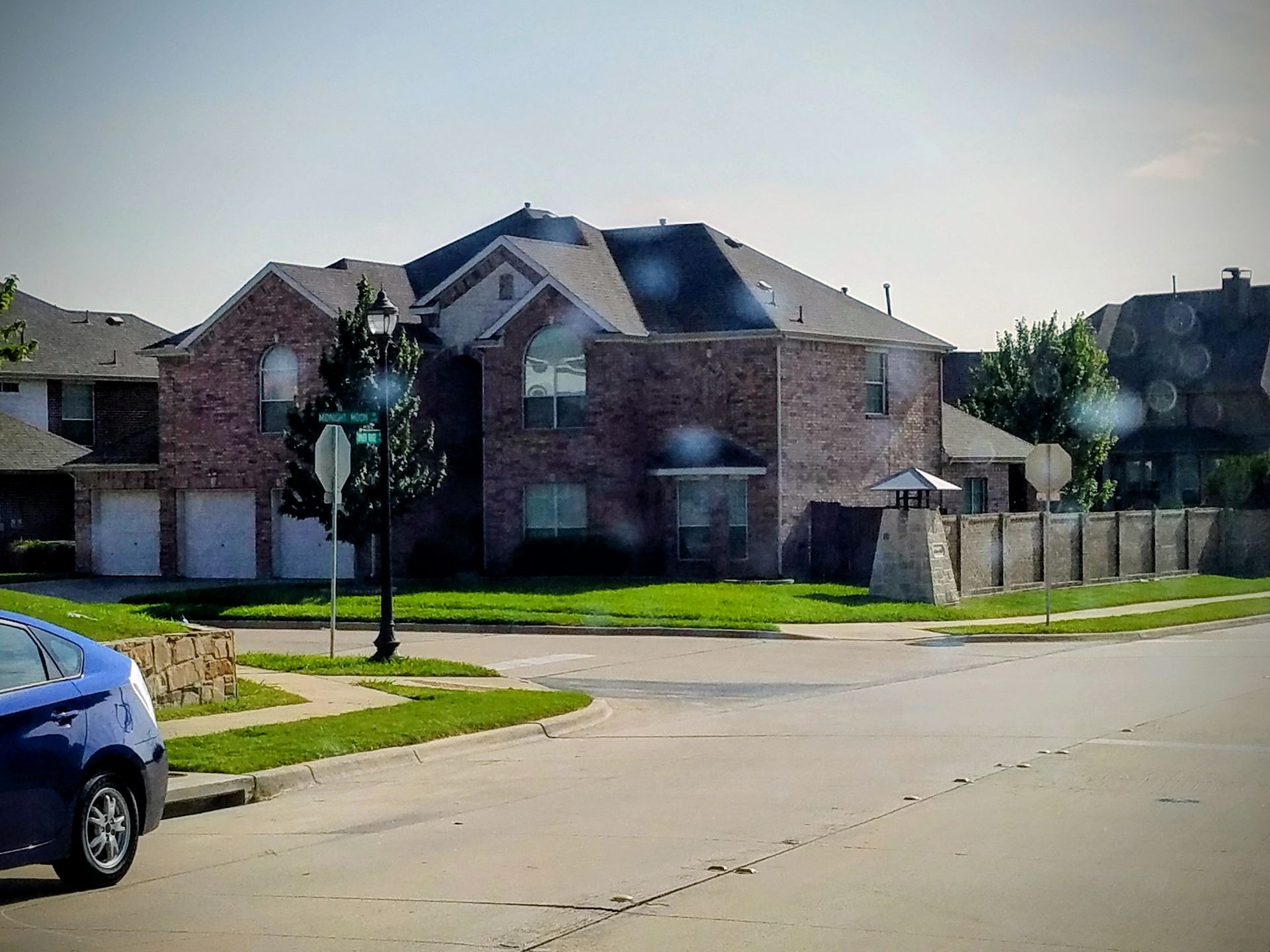 Brick house on a corner lot with a green lawn, two-car garage, and blue car parked in front.