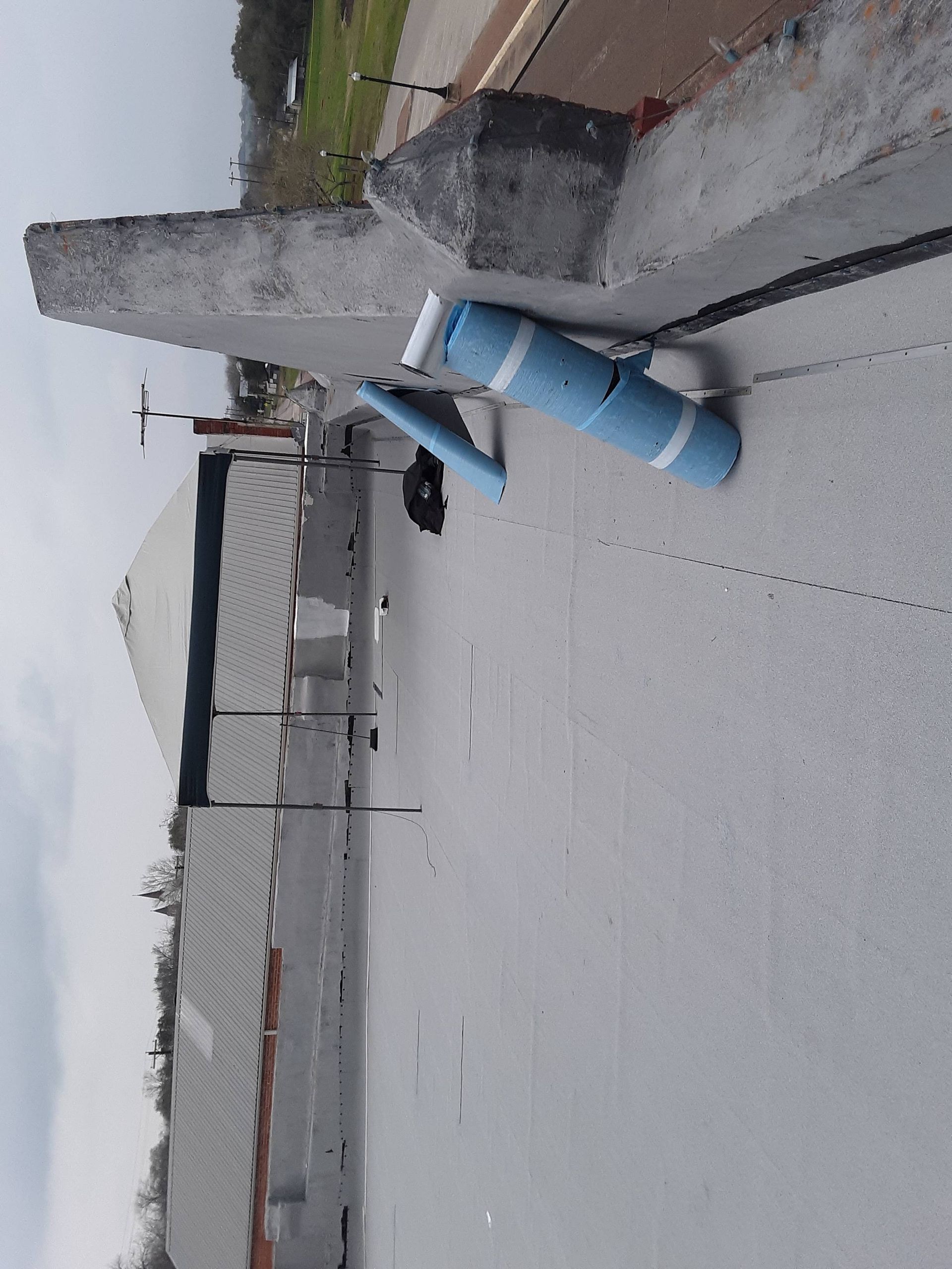 Flat roof with blue insulation rolls and building in the background. Cloudy sky.