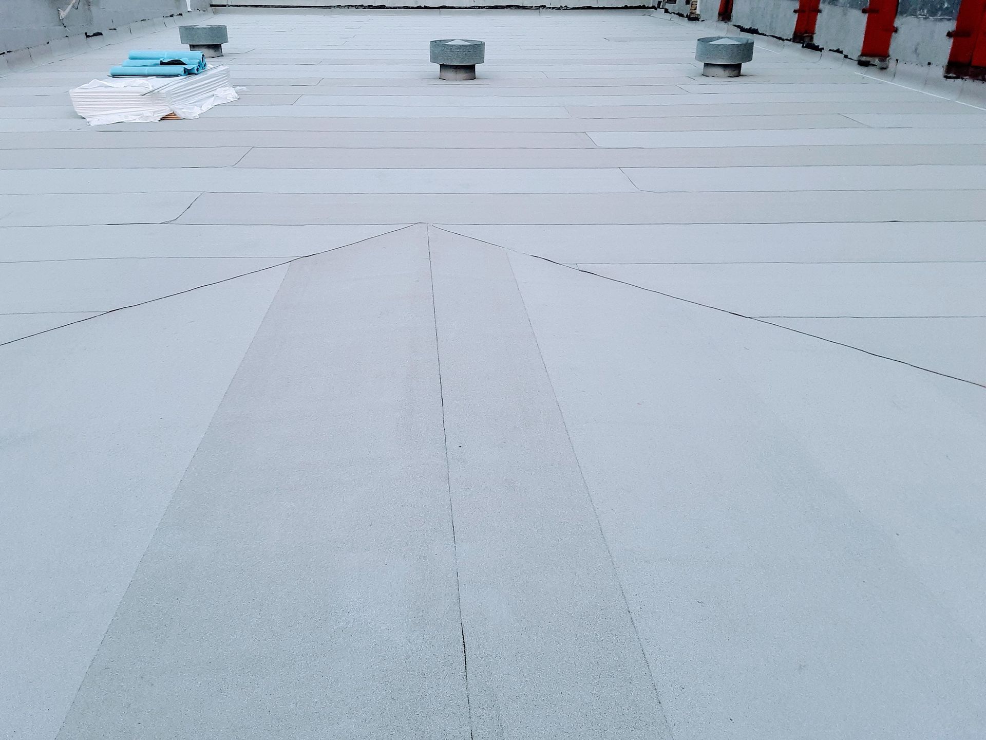 White commercial flat roof with air vents, seams, and debris.