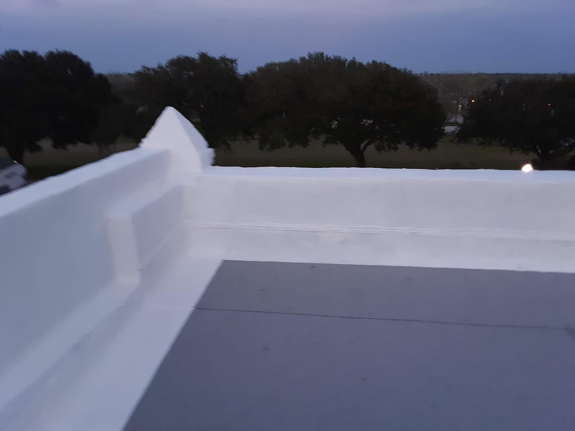 View from a white rooftop edge at dusk, with trees in the background.