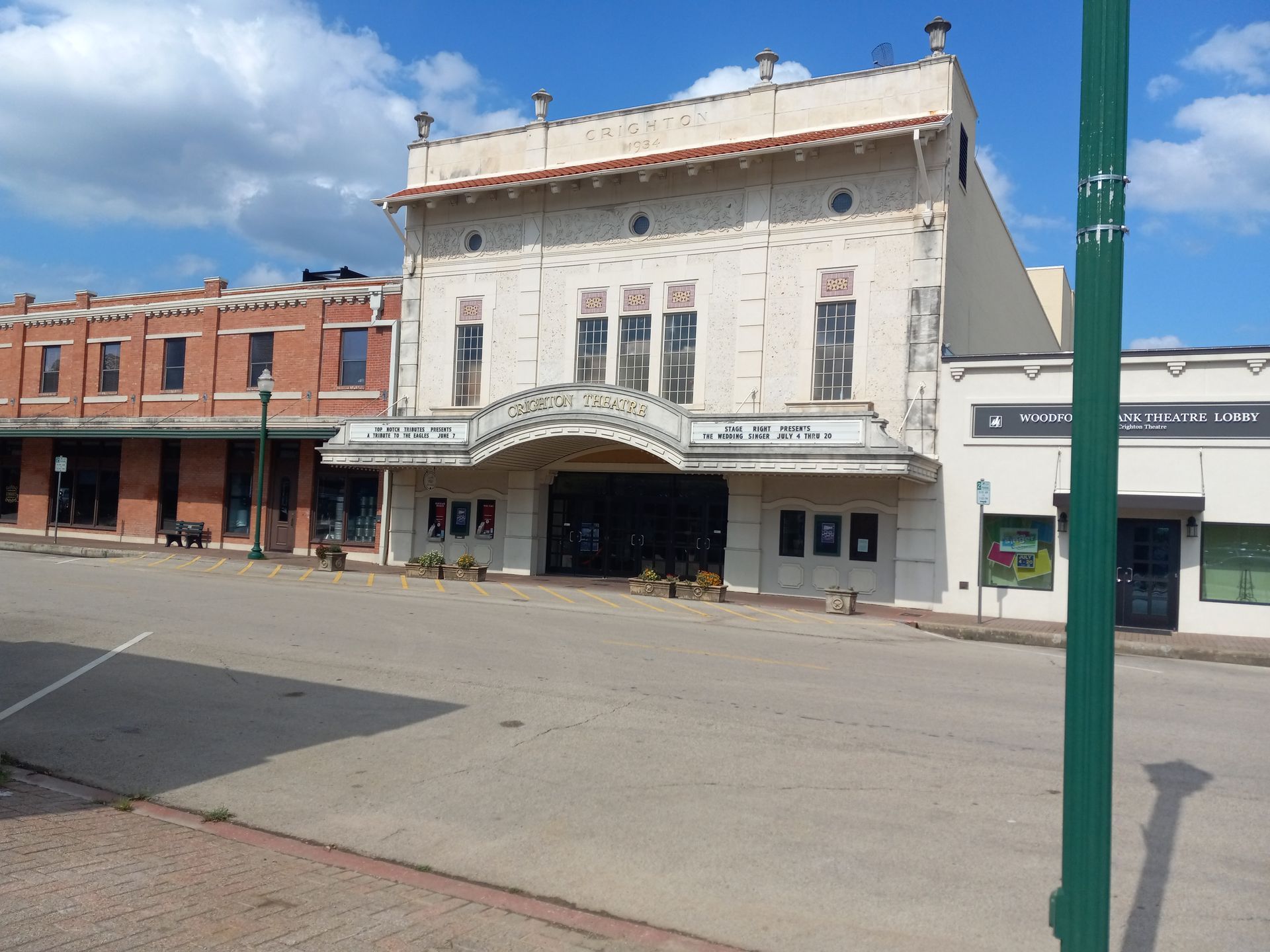 A two-story beige theater on a street, with a curved marquee and adjacent buildings.