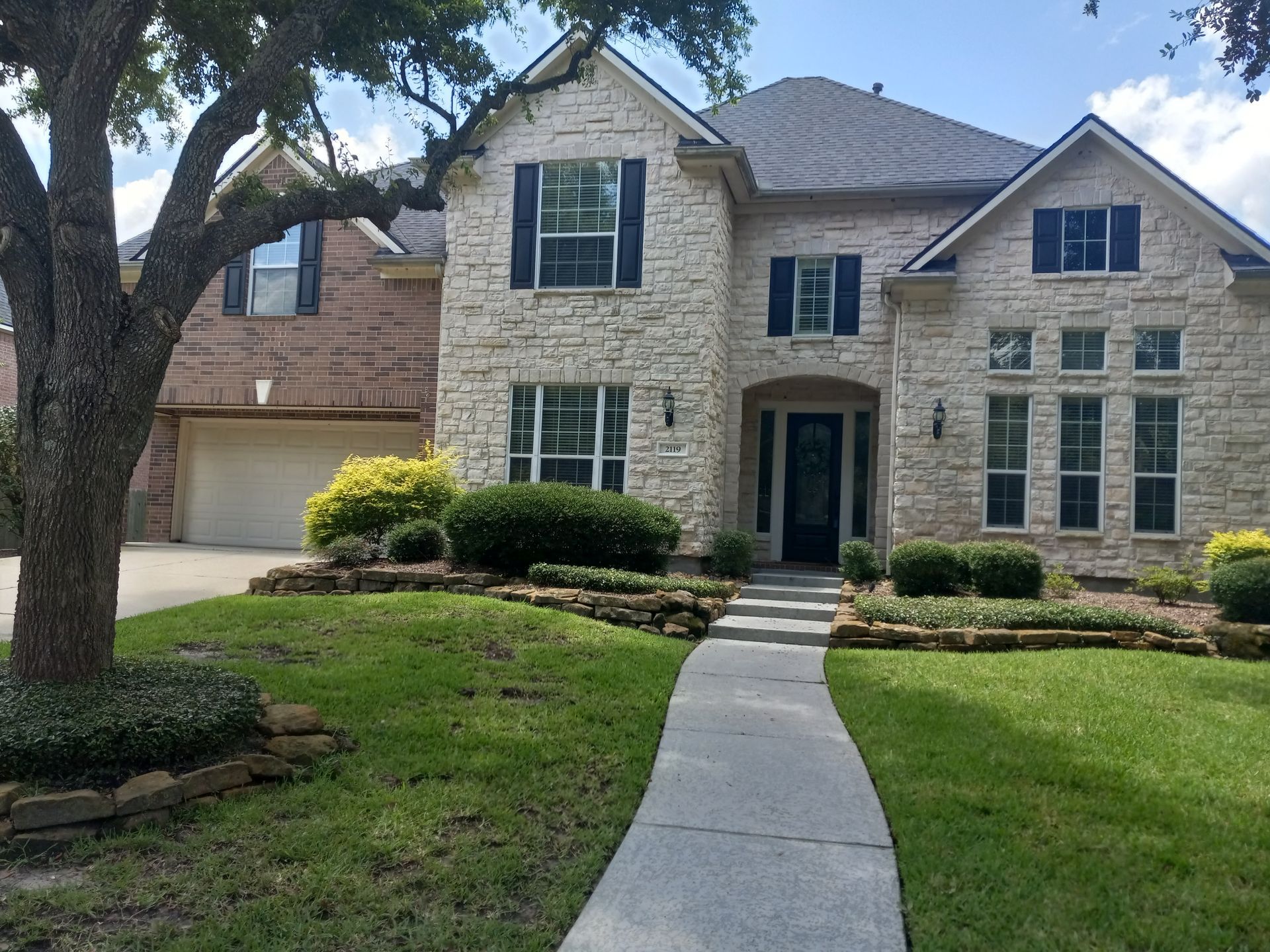 Stone and brick house with walkway, landscaping, and blue shutters.