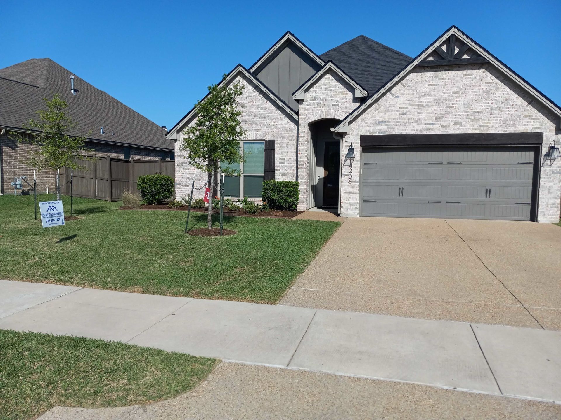 Suburban home with a gray garage door, brick facade, and well-kept lawn on a sunny day.