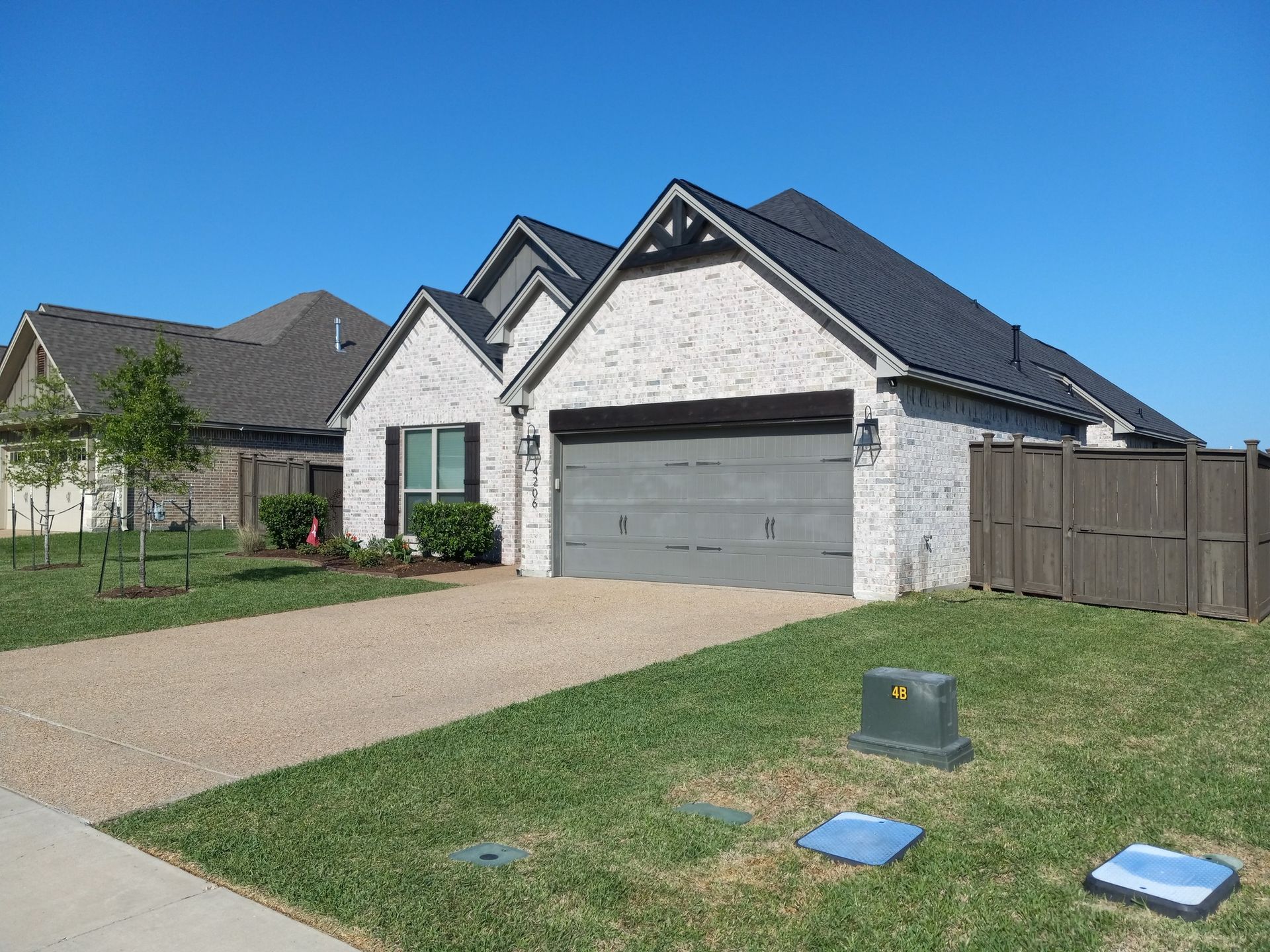 White brick house with gray garage door, driveway, lawn, and blue sky.