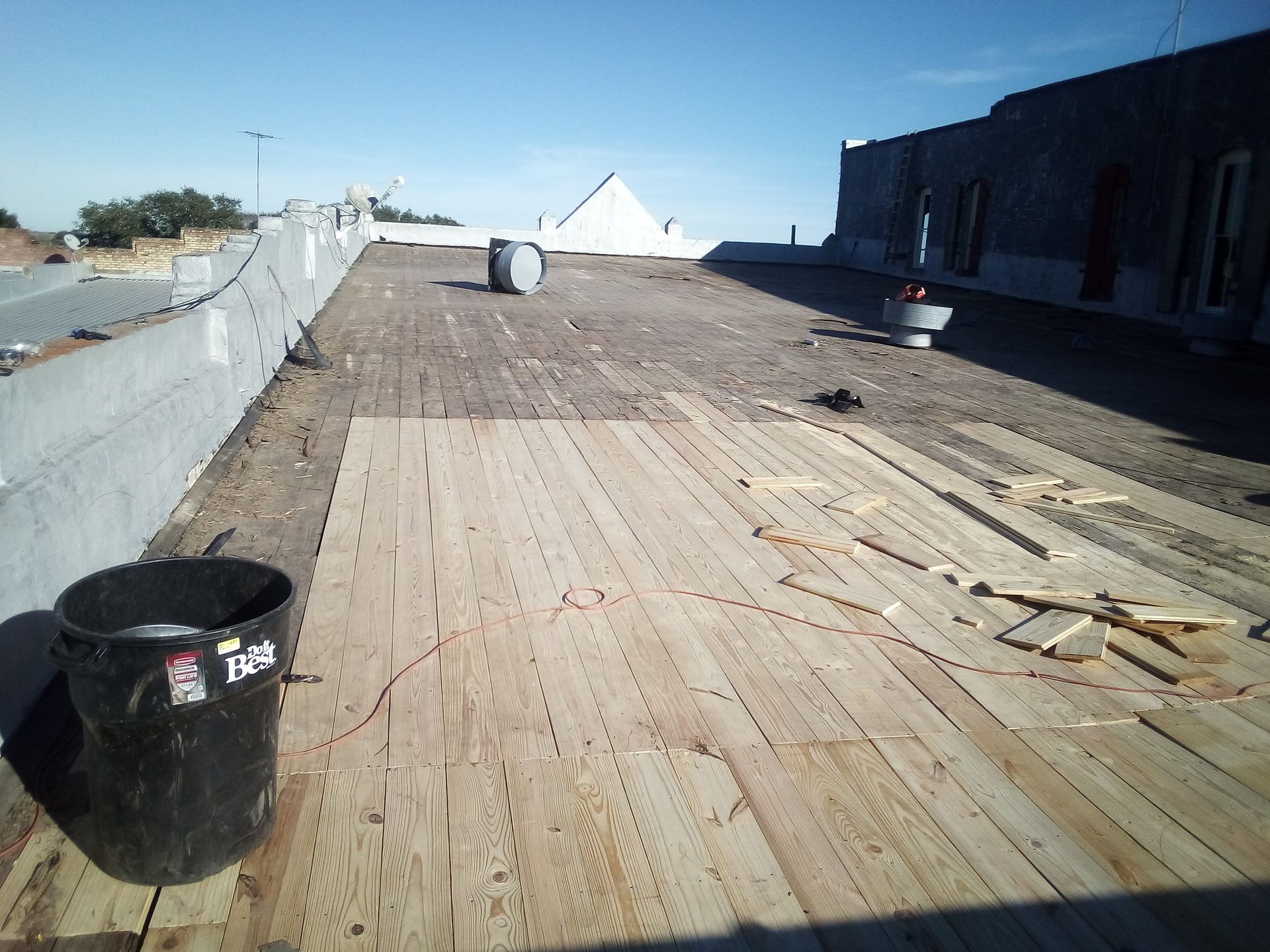 Wooden rooftop under construction, black bucket in foreground, clear sky.