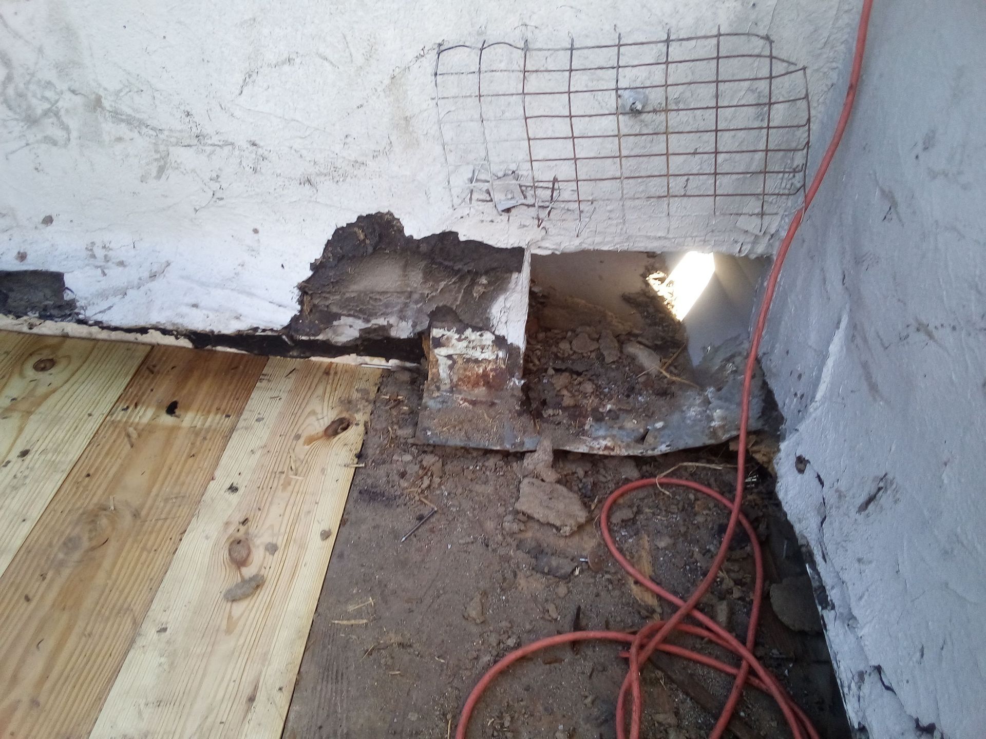 Damaged foundation wall with exposed brick, earth, and new wooden floorboards.