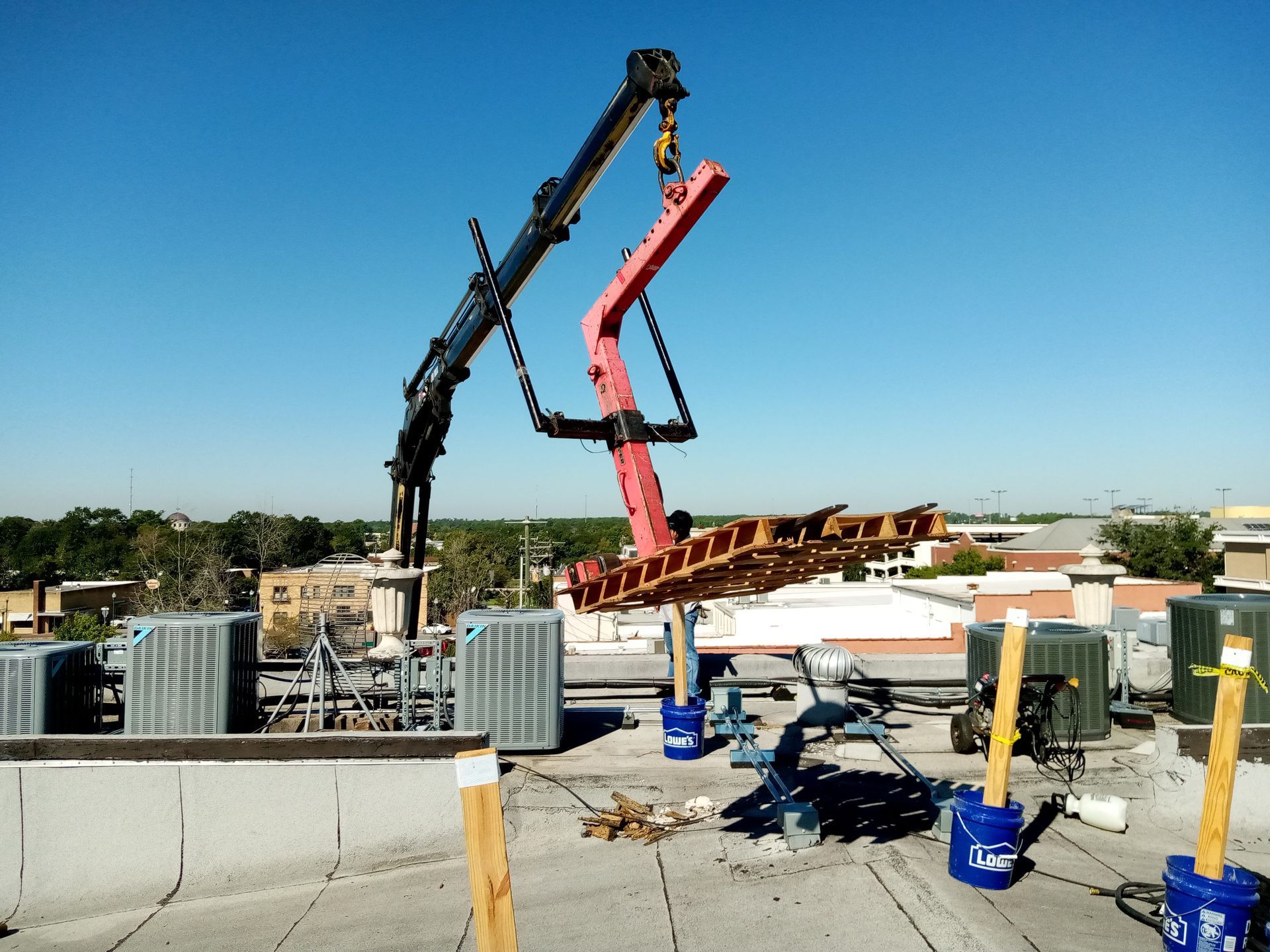 A crane lifting a red and brown structure onto a flat rooftop on a sunny day.