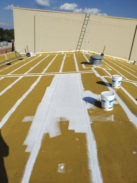 White sealant applied on yellow roof. Buckets and ladder visible. Exterior daylight.