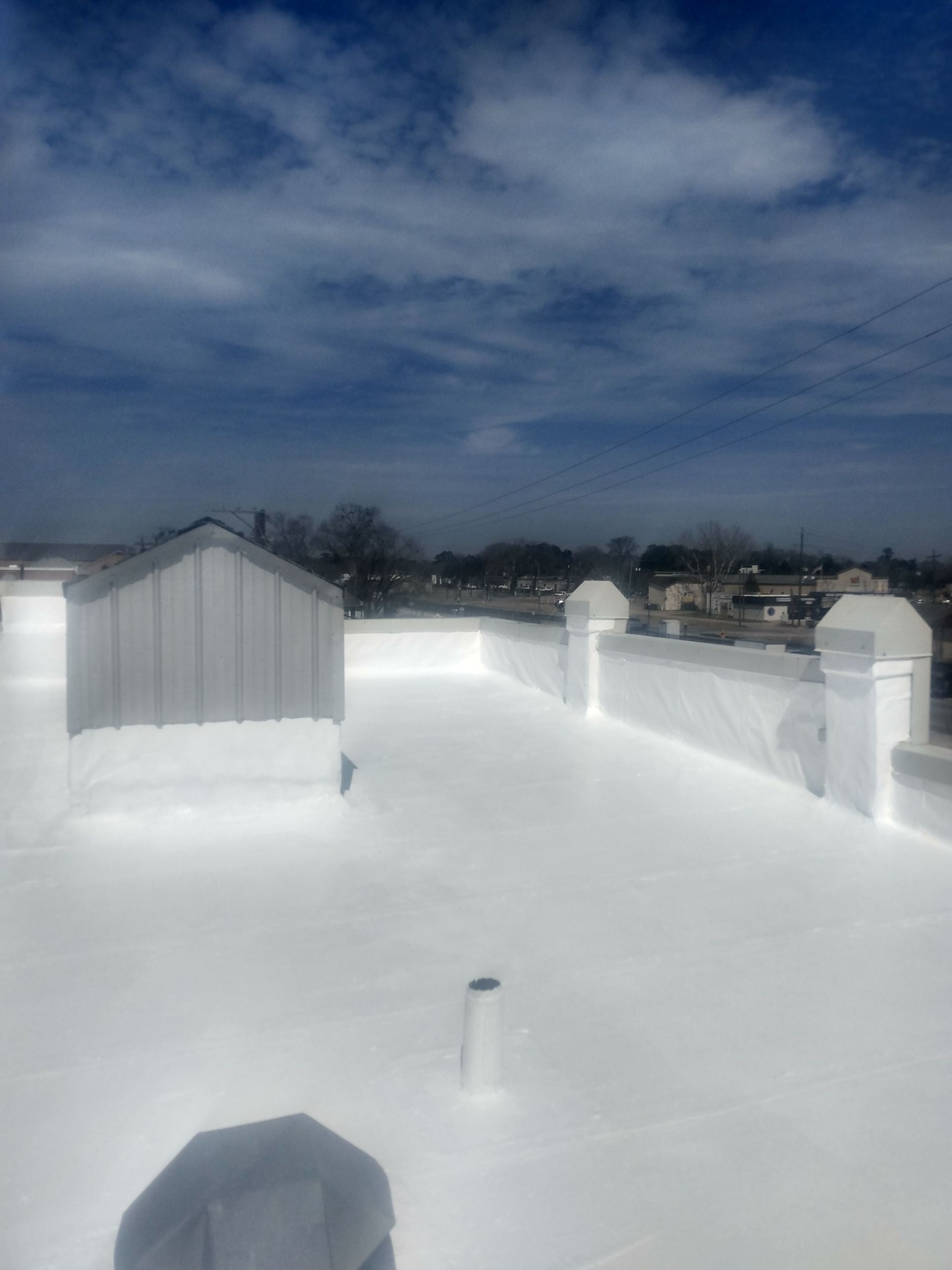 White flat roof with a light blue sky. Building in the background.