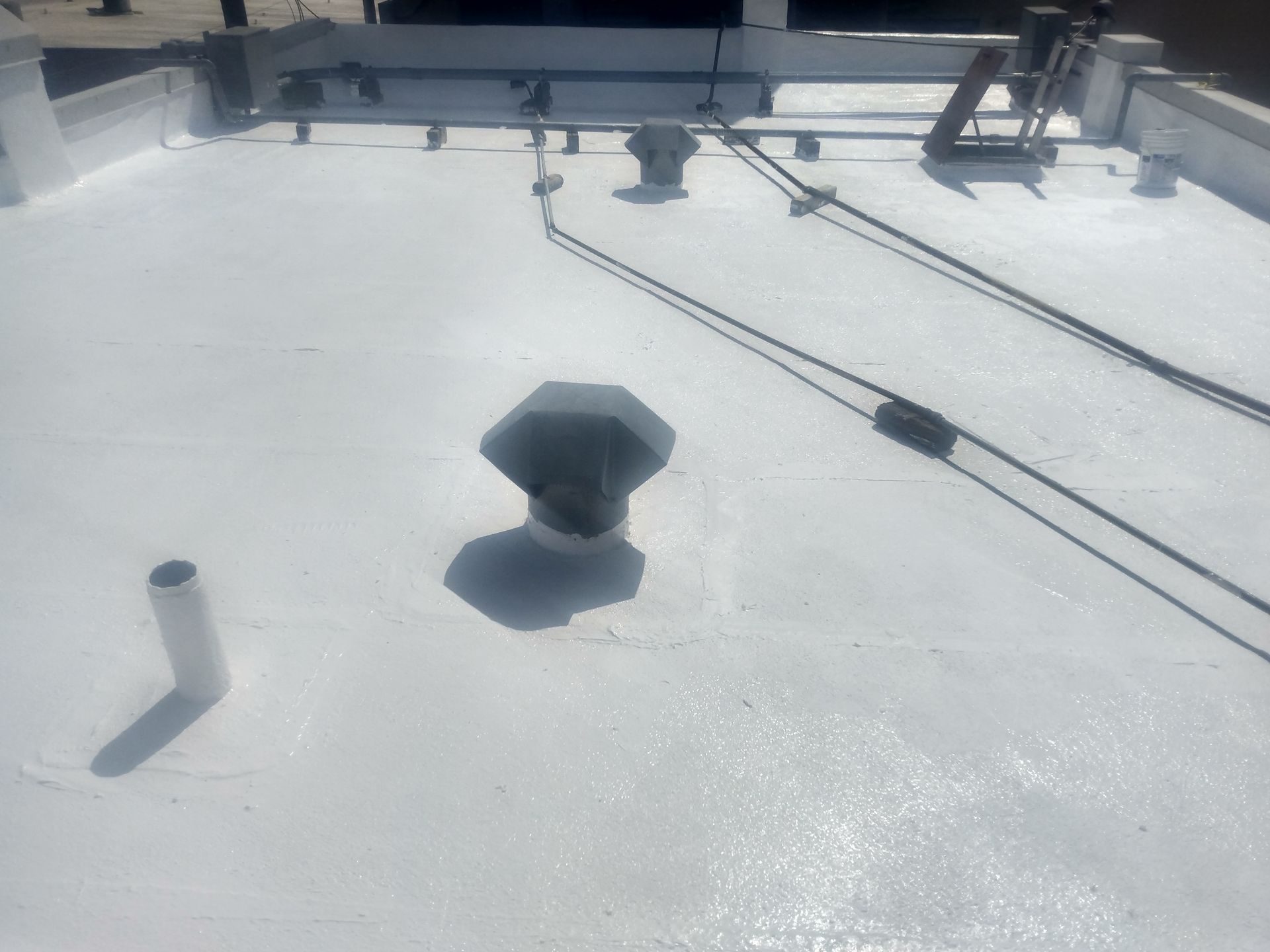 White commercial rooftop with vent, pipes, and cables.