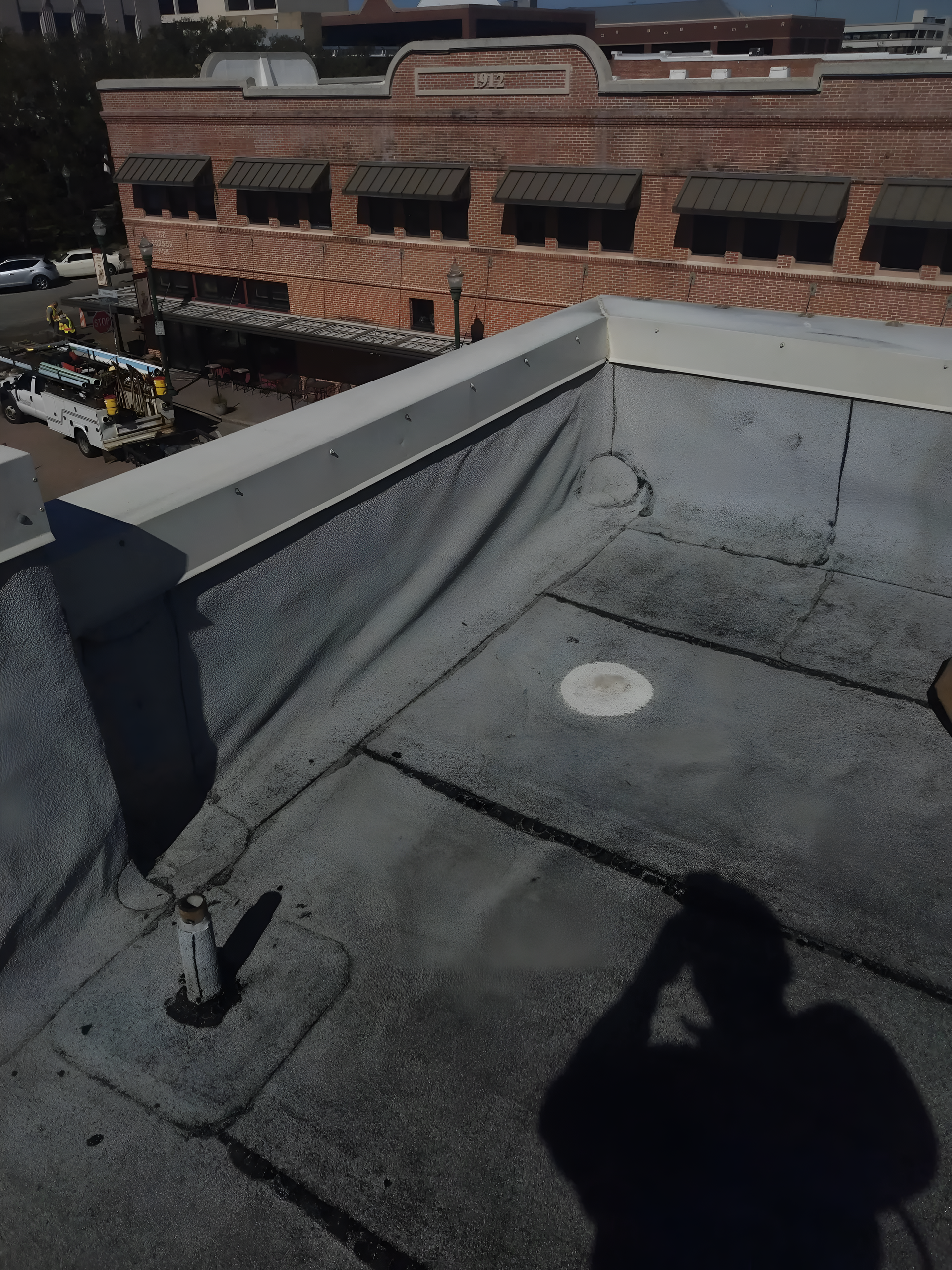 Rooftop with a gray surface, white trim, and a building in the background. A person's shadow is cast on the roof.