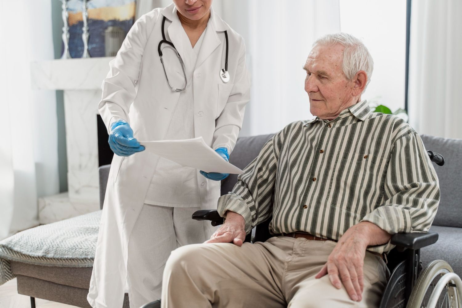 Doctor shows paperwork to elderly man in wheelchair, indoors.