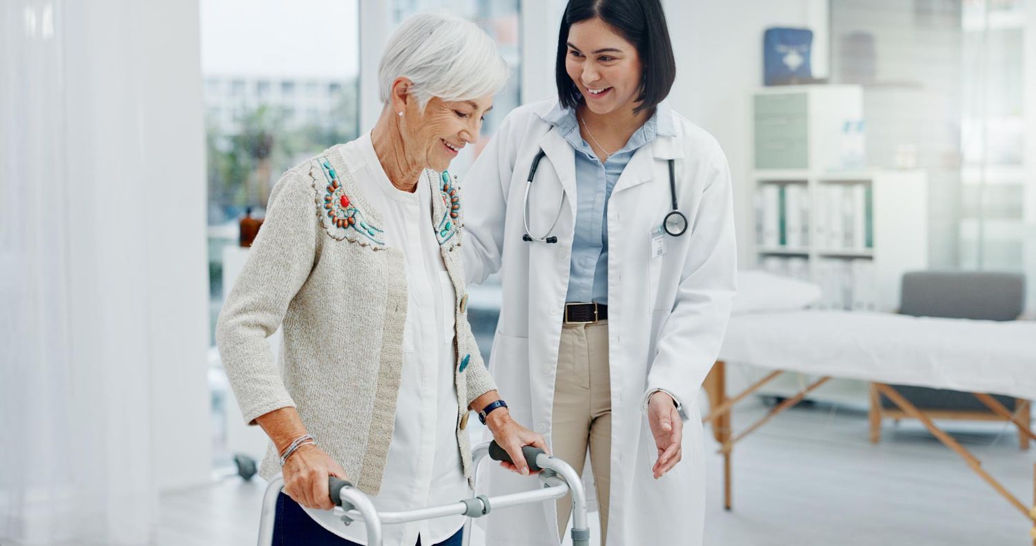 Doctor assists elderly woman using a walker in a bright medical office.