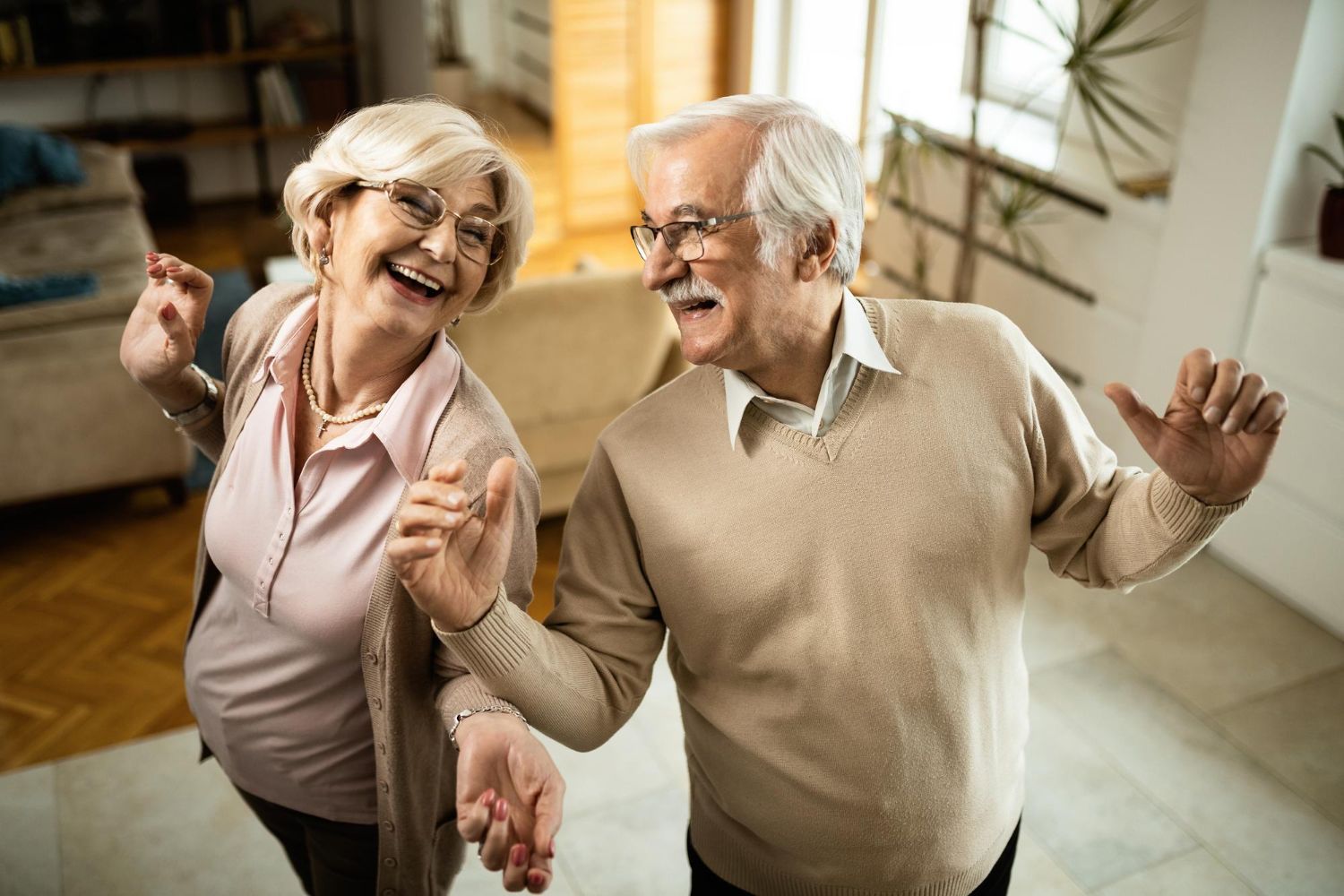 Smiling elderly couple dancing in their living room.