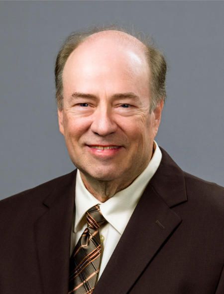 A bald man in a suit and tie smiles for the camera