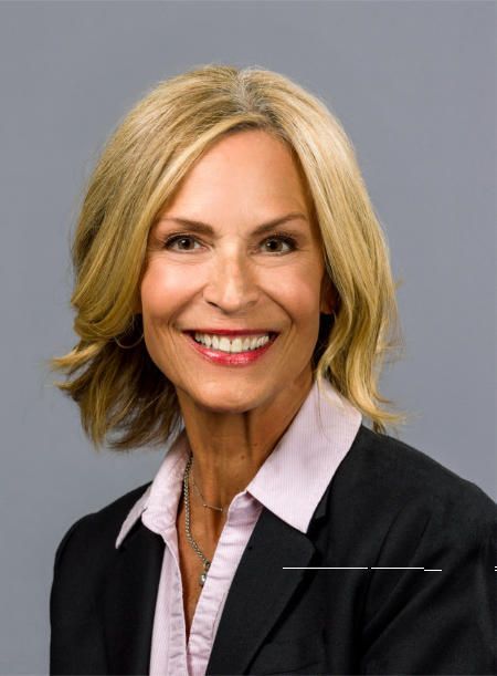 A woman in a suit and pink shirt smiles for the camera
