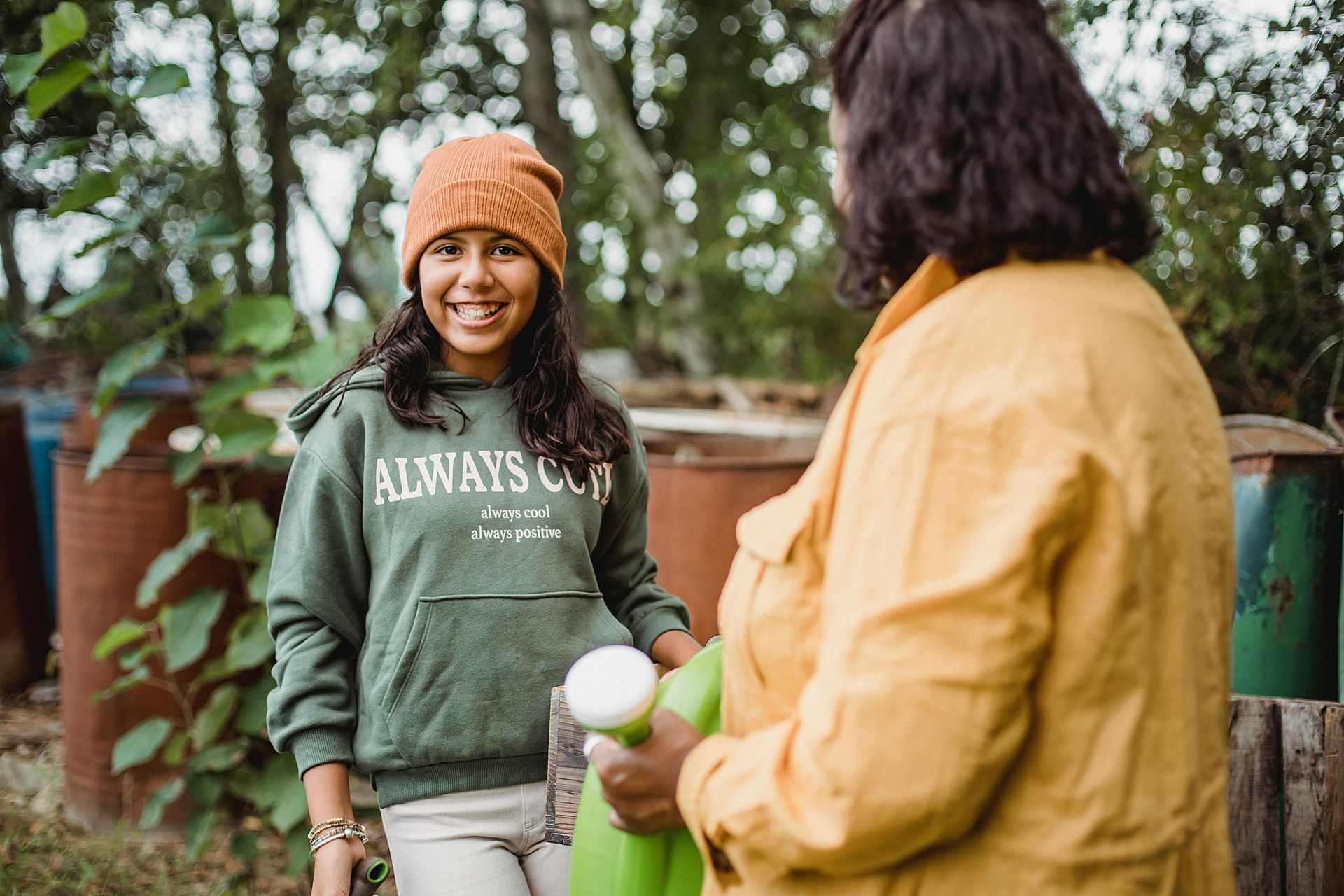 A woman is holding a green watering can and talking to a young girl.