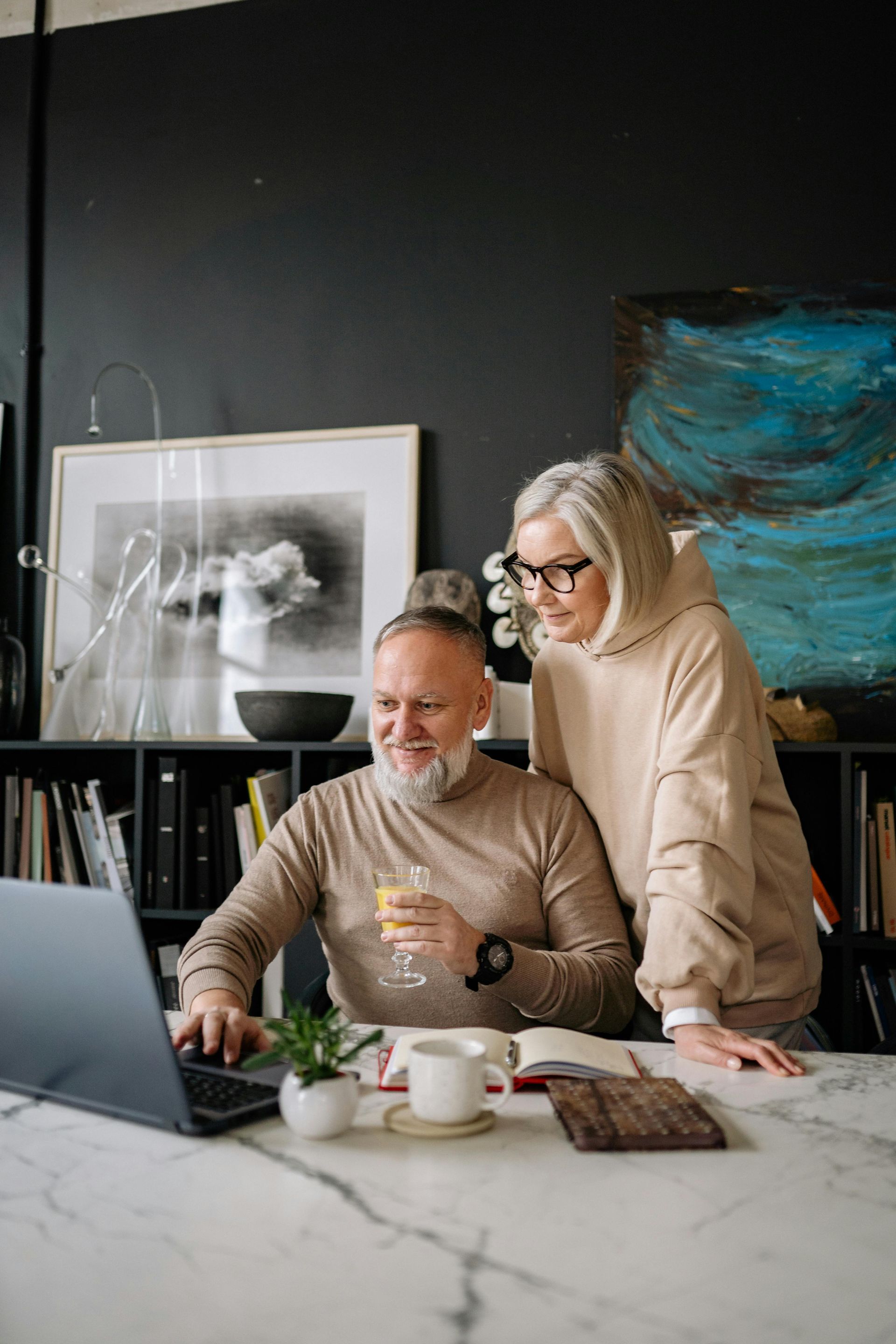 Senior couple looking at laptop screen together; smiling. Indoors, well-lit.