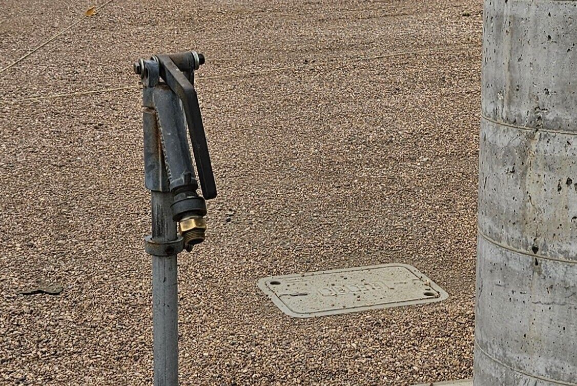 A hose is attached to a metal pole in a gravel area.
