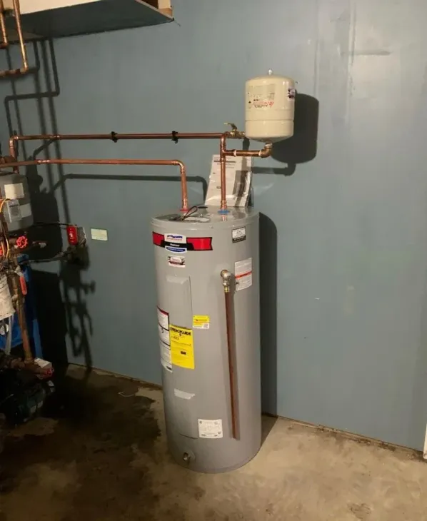 A gray water heater with copper pipes against a blue wall in a basement setting.