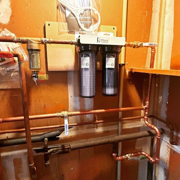 Copper pipes with a dual water filter system mounted on an orange wall.