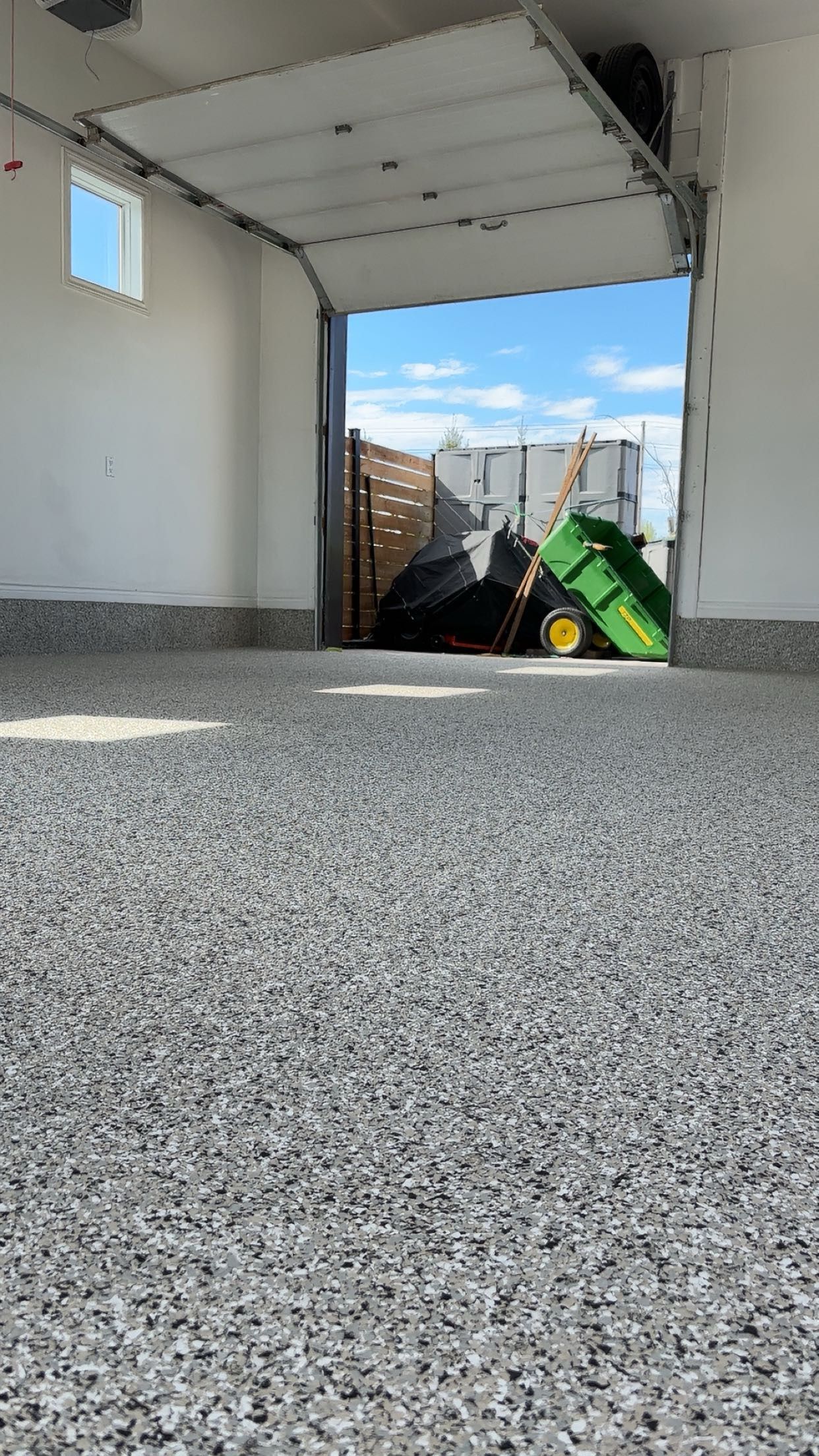 A garage with a green toy tractor in it and a garage door open.