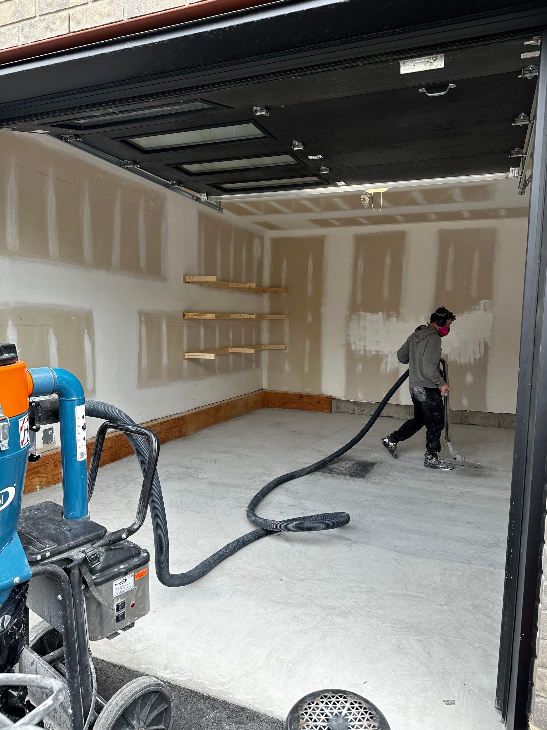 A man is using a vacuum cleaner to clean a garage floor.