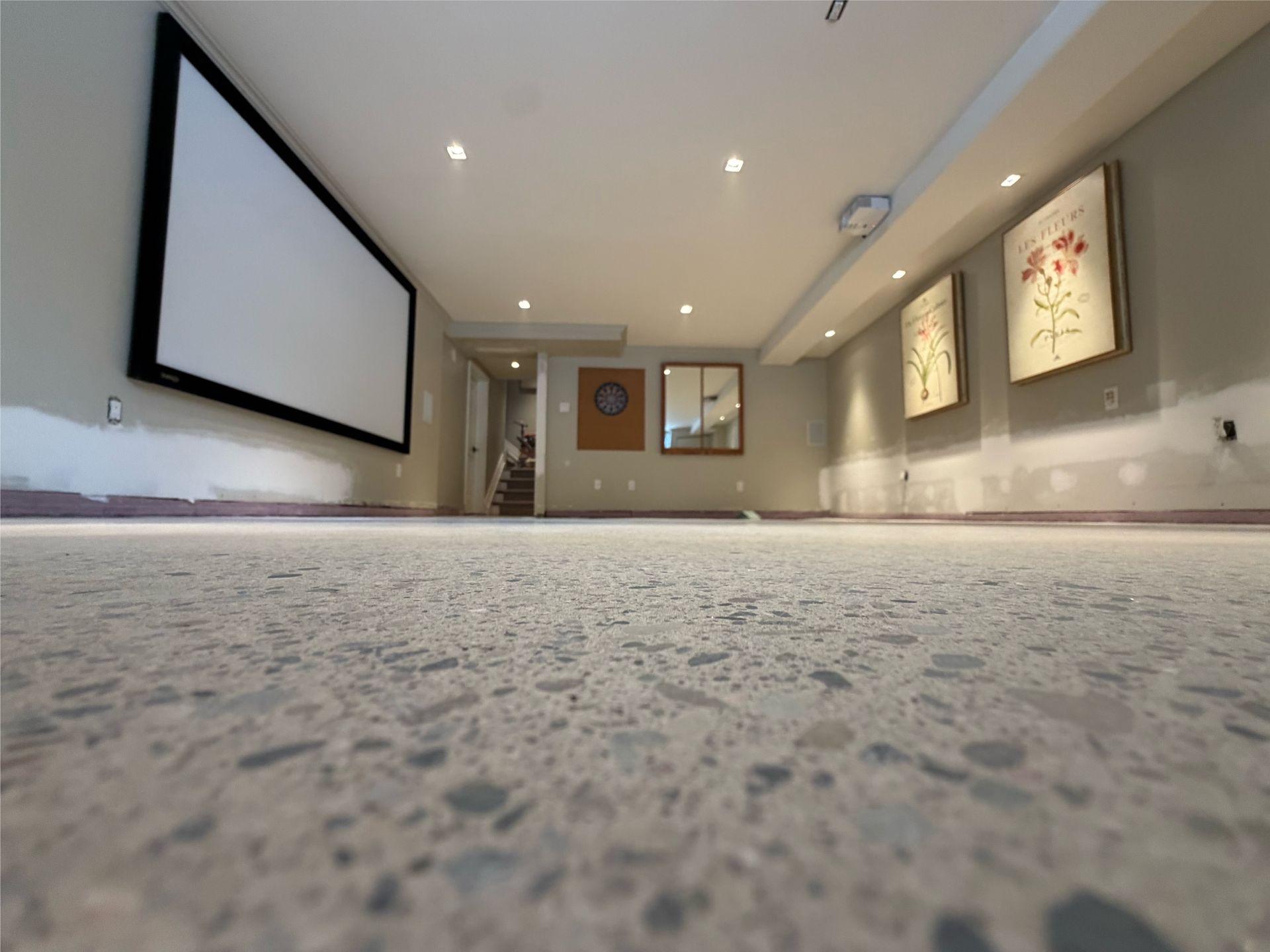 Finished basement with shiny, speckled floor, exposed utilities, and concrete walls.