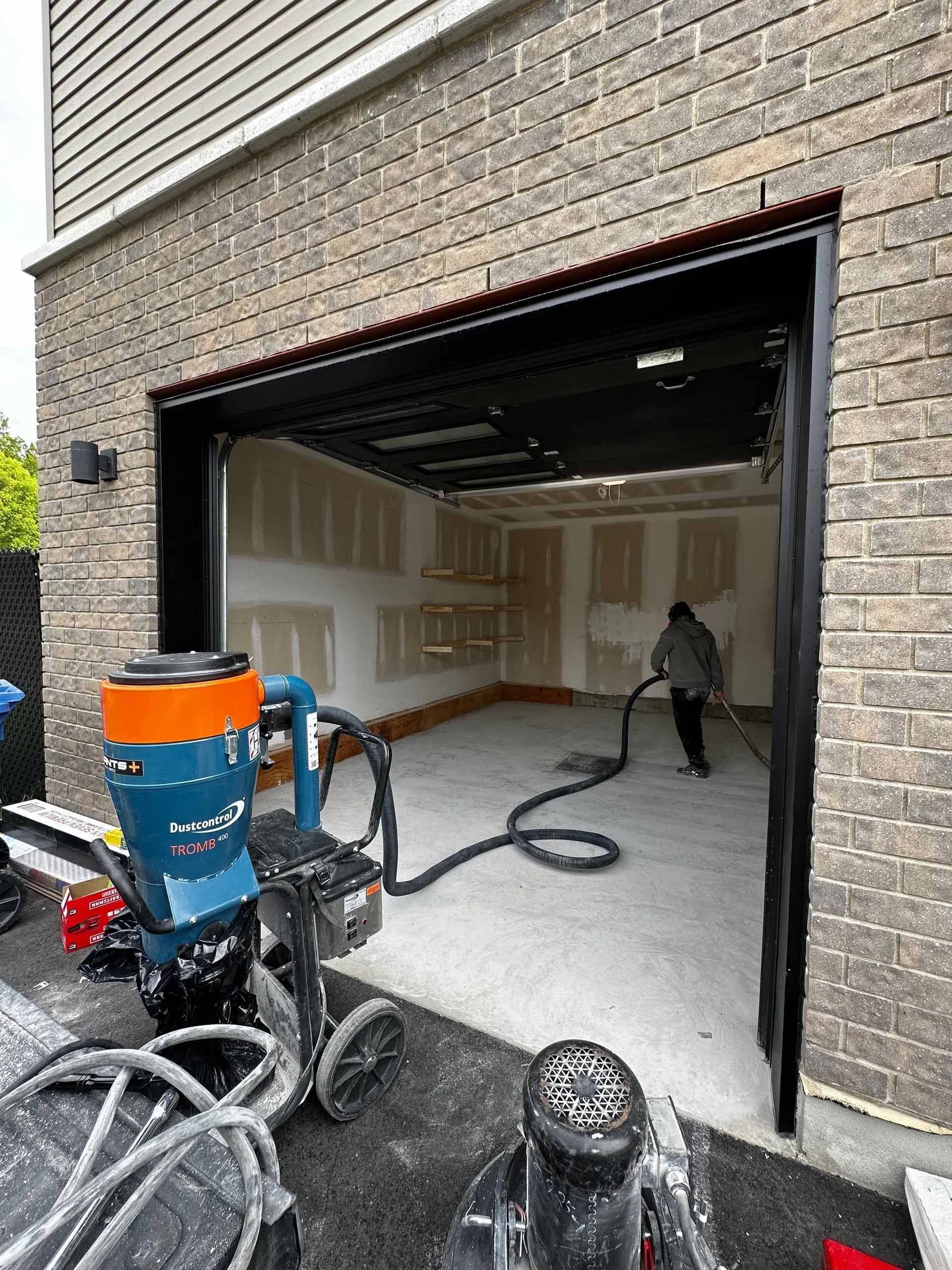 A man is cleaning the floor of a garage with a vacuum cleaner.
