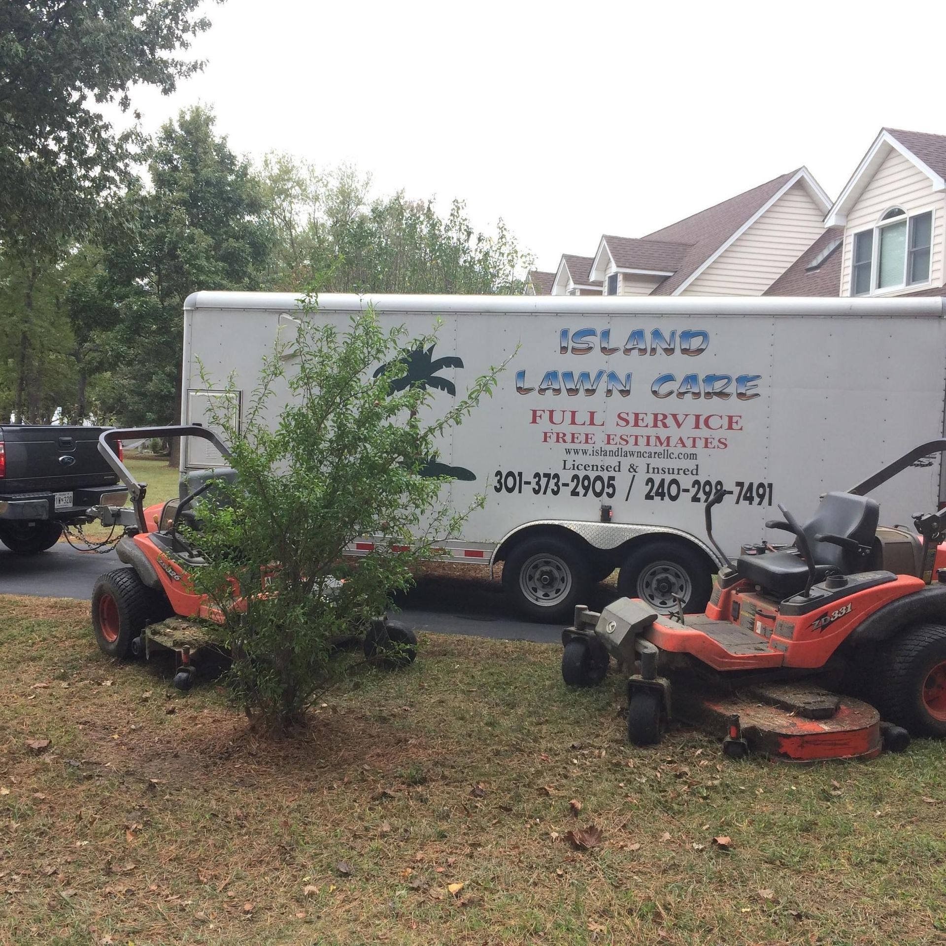 Two lawn mowers are parked in front of an island lawn care trailer