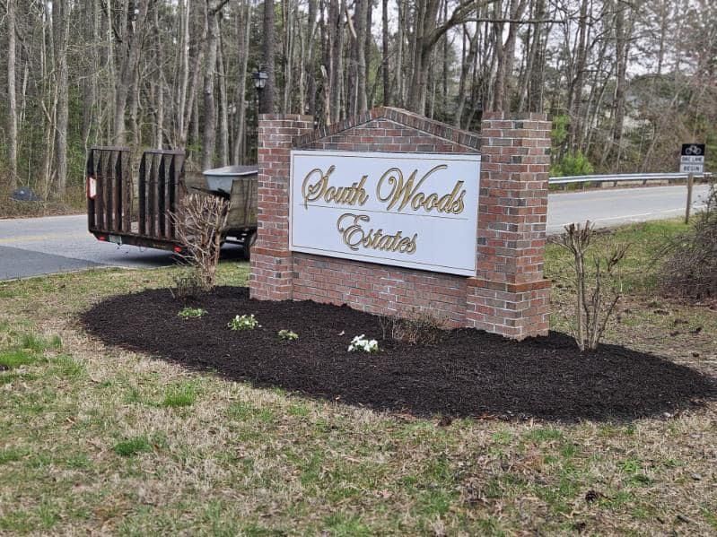 A sign for south woods estates is in the middle of a lush green field.