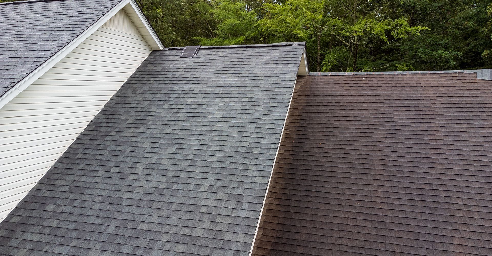 A black and brown roof on a house with trees in the background.