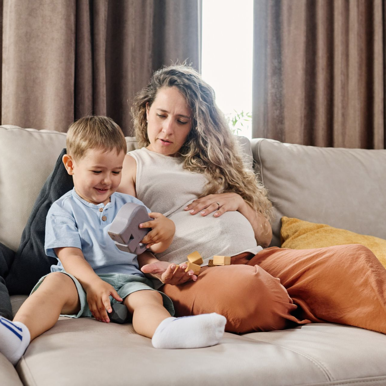 Pregnant woman and child sitting on a sofa, playing with a toy.