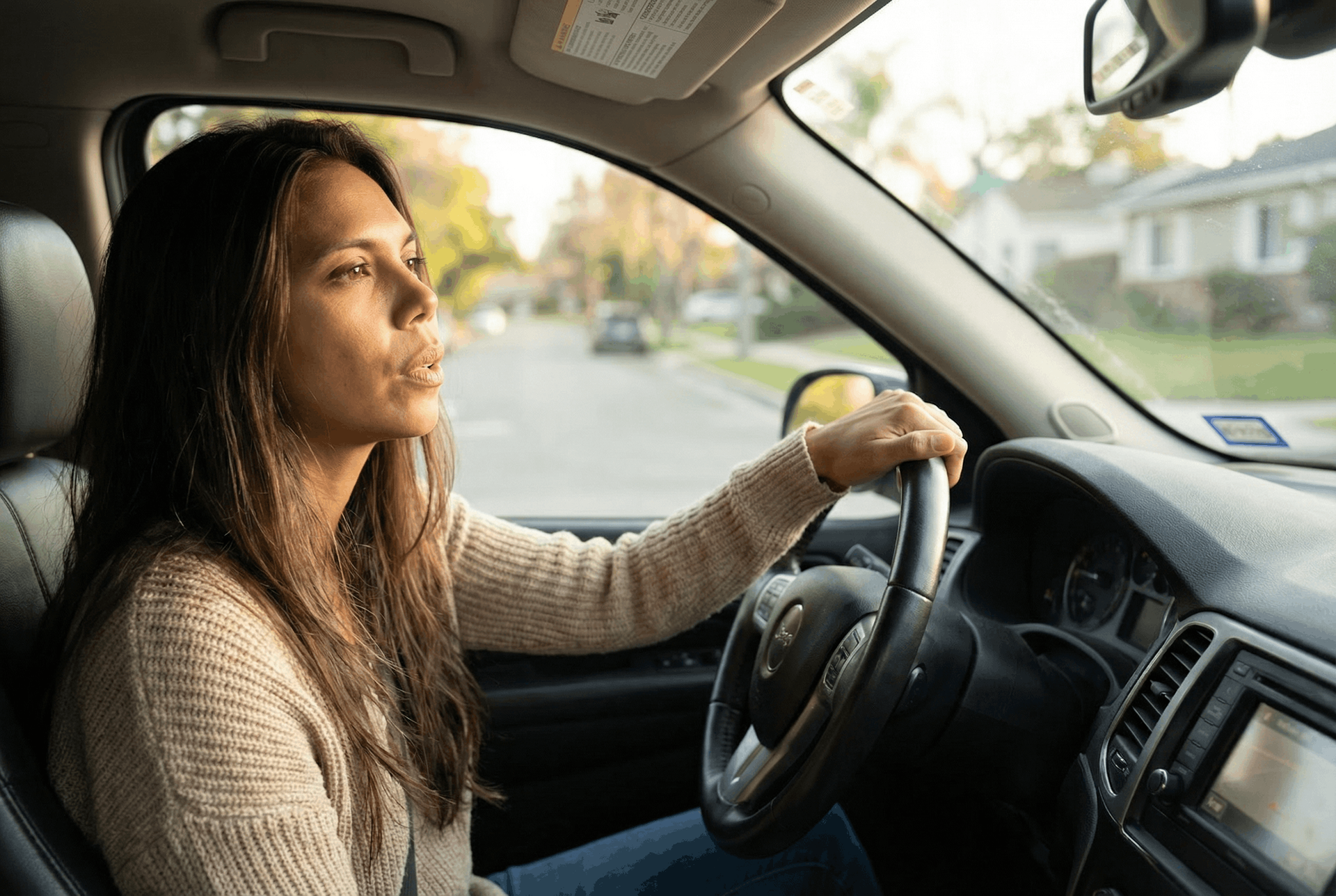 Woman driving a car, looking out the windshield. Interior view, sunny day.