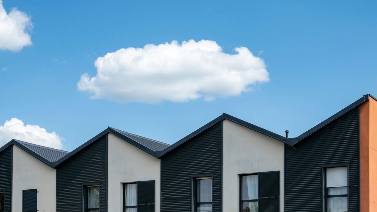 Row of modern houses with repeating triangular roofs, contrasting black and white panels, against a bright blue sky.