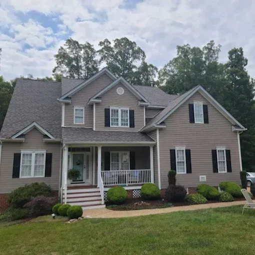A two-story grey vinyl-sided house with a covered front porch, dark shutters, and a landscaped yard.