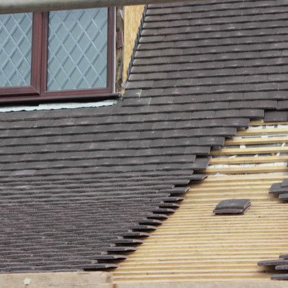 A section of a roof partially covered in dark tiles, with the wooden support structure exposed on the right side.
