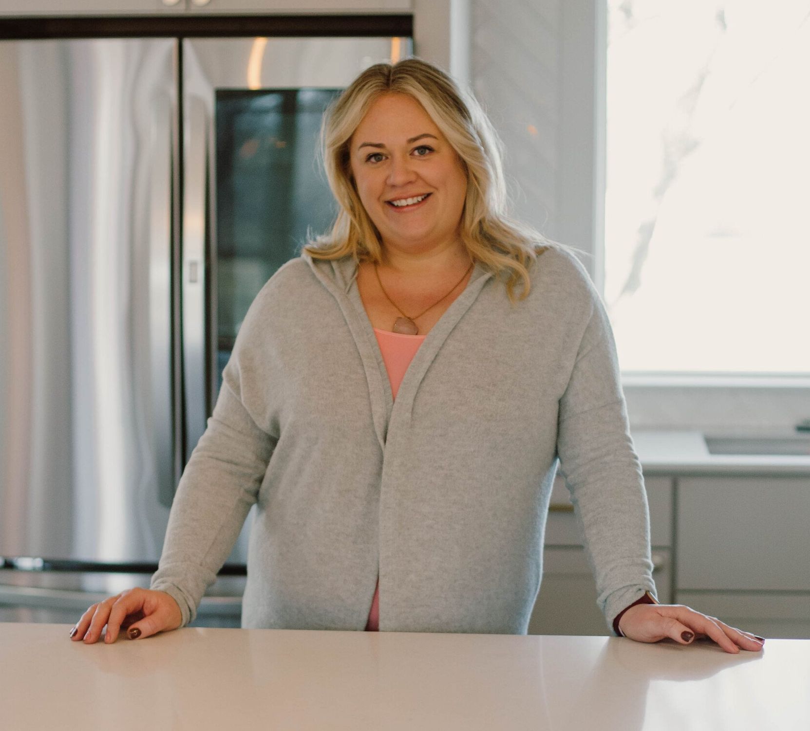 A woman in a grey sweater is leaning on a counter in a kitchen