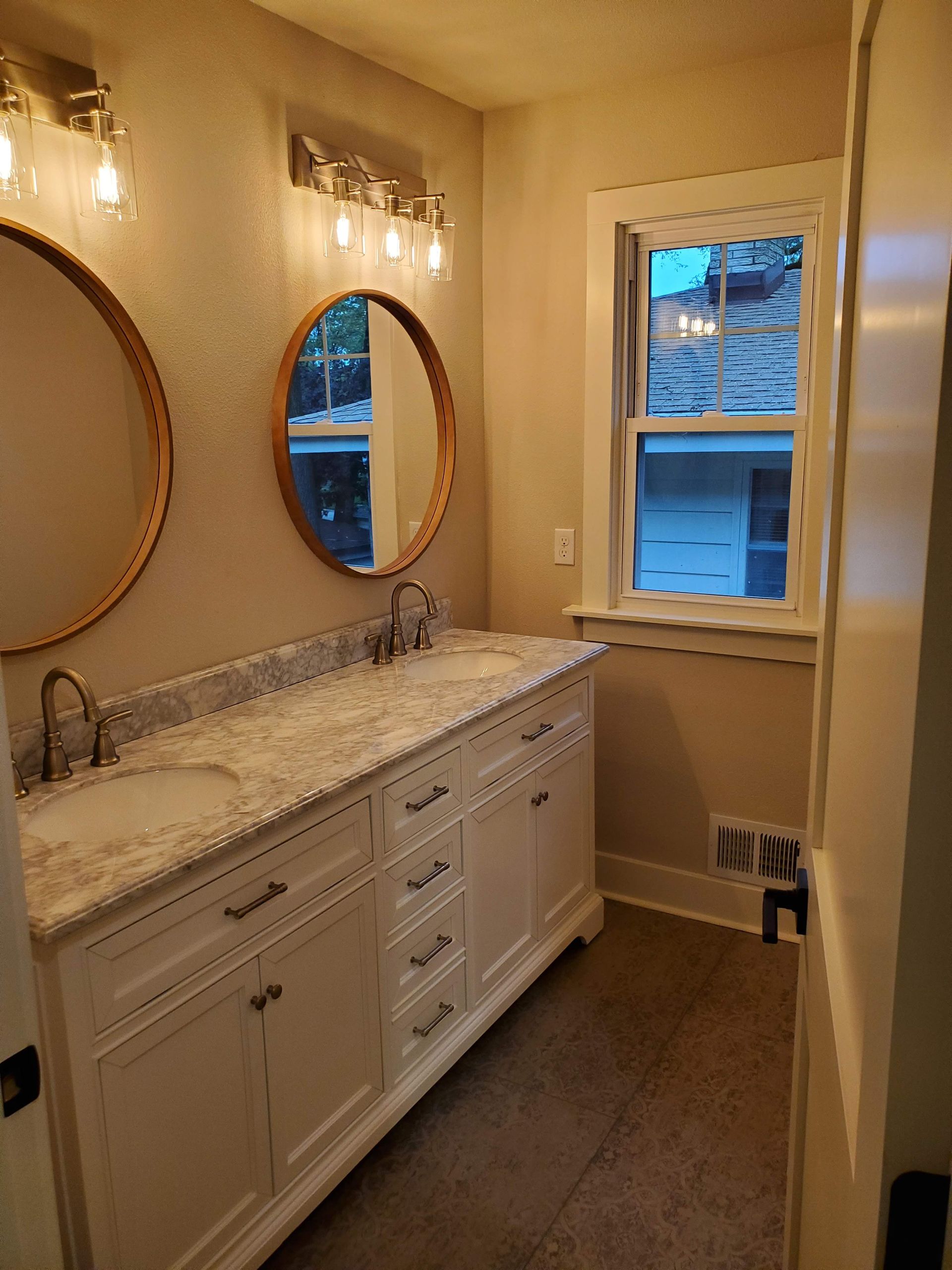 a bathroom with two sinks , two mirrors and a window .