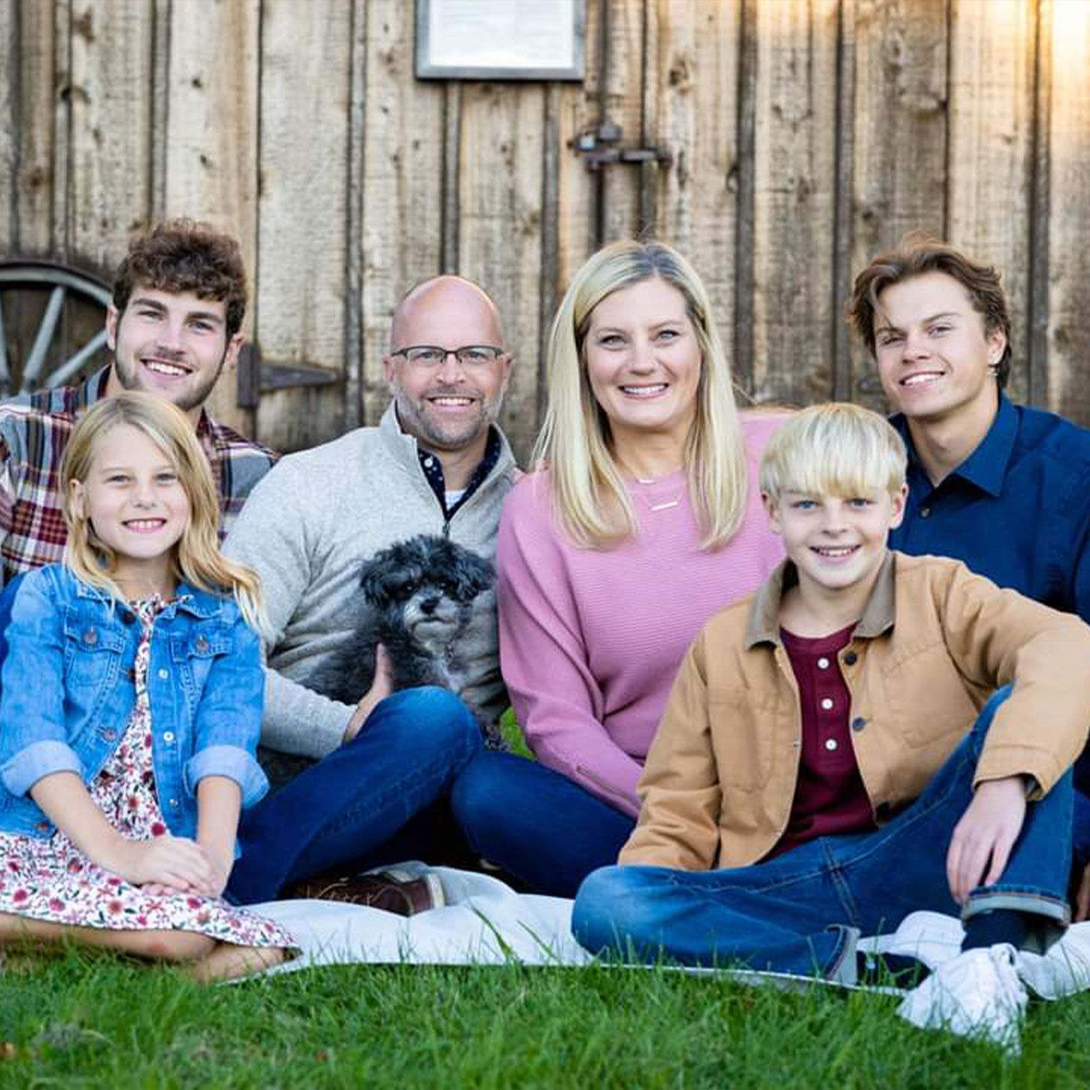 a family is posing for a picture while sitting in the grass with a dog .