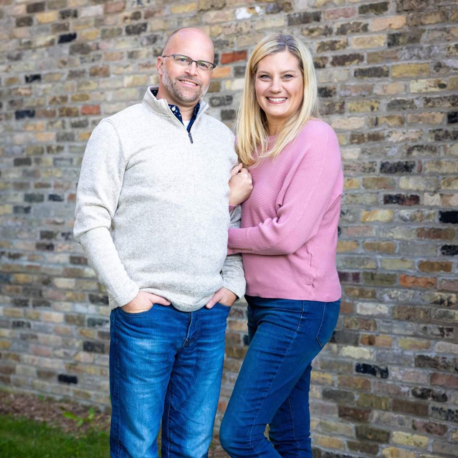a man and a woman are posing for a picture in front of a brick wall .