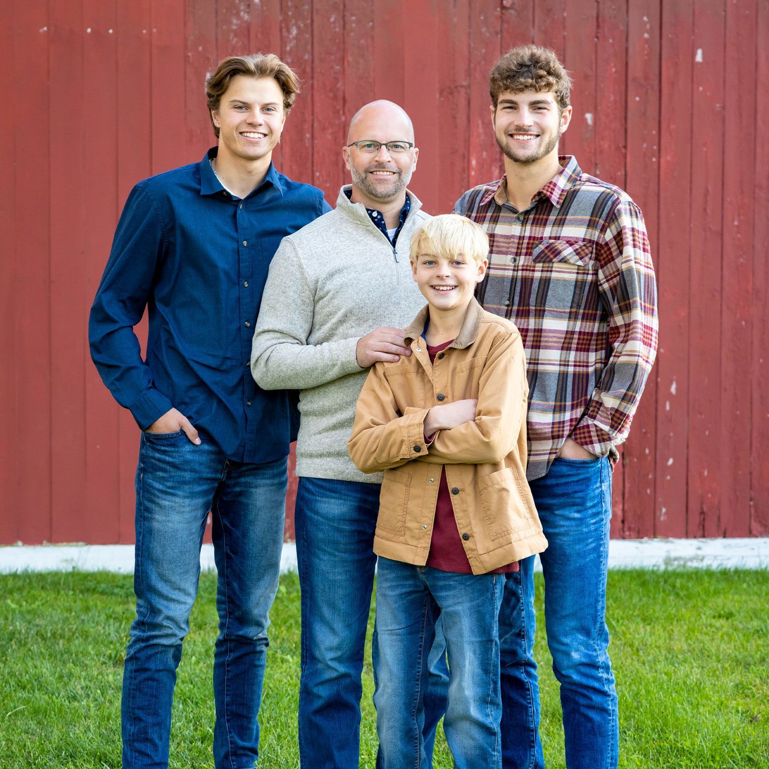 three men and a boy are posing for a picture in front of a red barn .