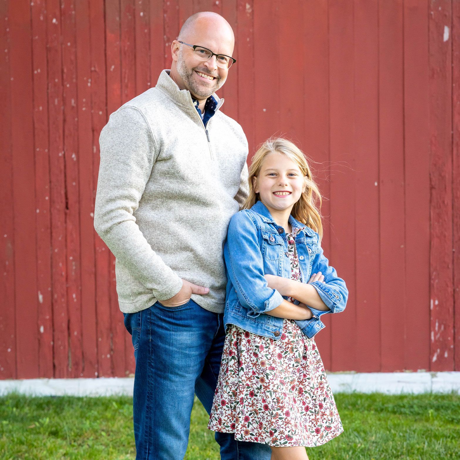 a man and a little girl are posing for a picture in front of a red barn .