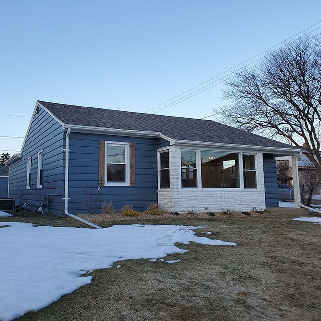 a blue and white house with snow on the ground in front of it .