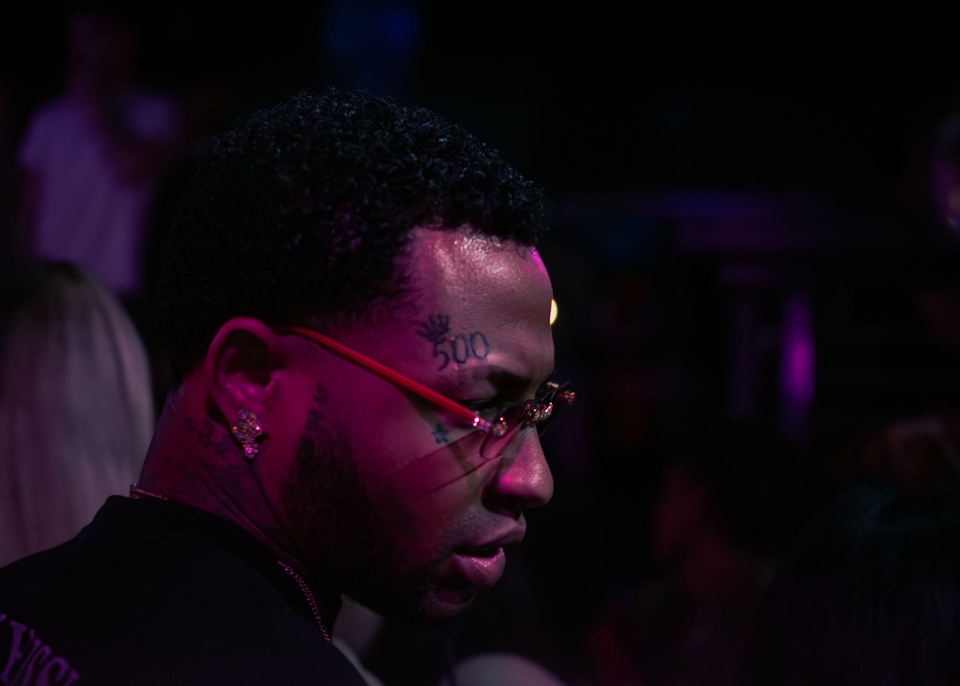 A man with a tattoo on his face is wearing glasses in a dark room. Trevion500