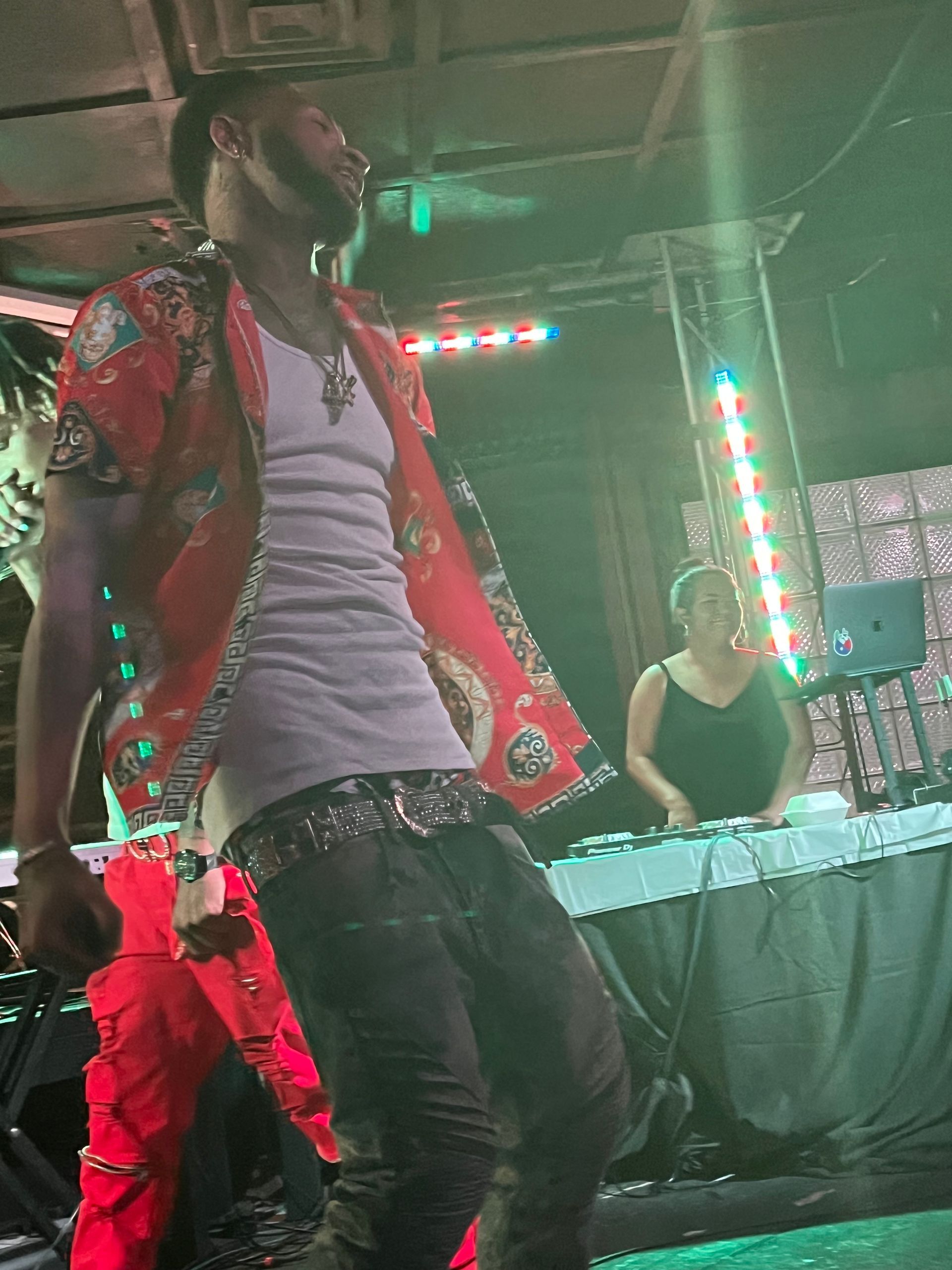 A man in a red shirt is standing on a stage in front of a DJ. Trevion500