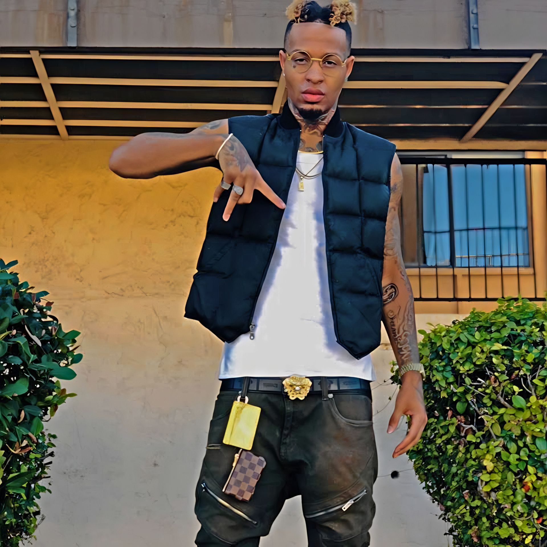 A man wearing a black vest and a white shirt is standing in front of a building. Trevion500