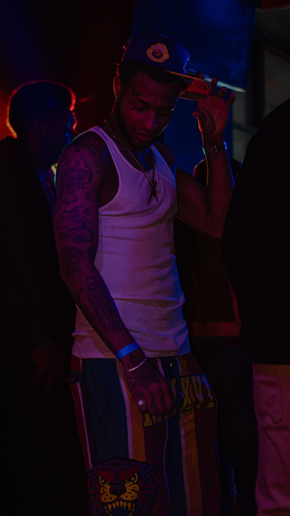 A man wearing a hat and a tank top is standing in a dark room. Trevion500